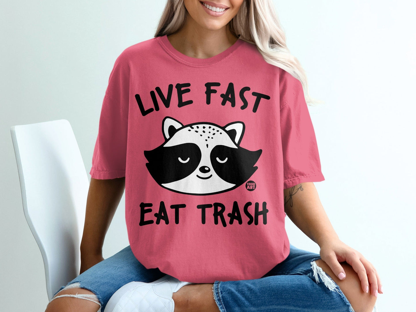 Pink t-shirt with raccoon graphic and text "LIVE FAST EAT TRASH".