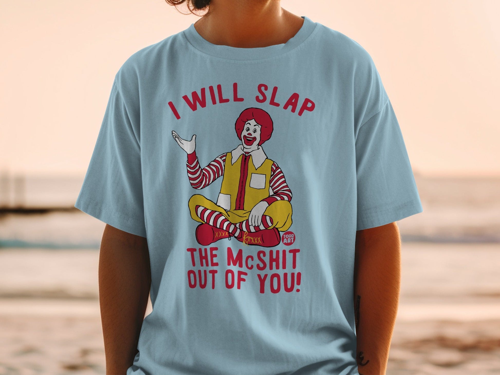 Ronald McDonald sitting cross-legged on a light blue t-shirt with text.
