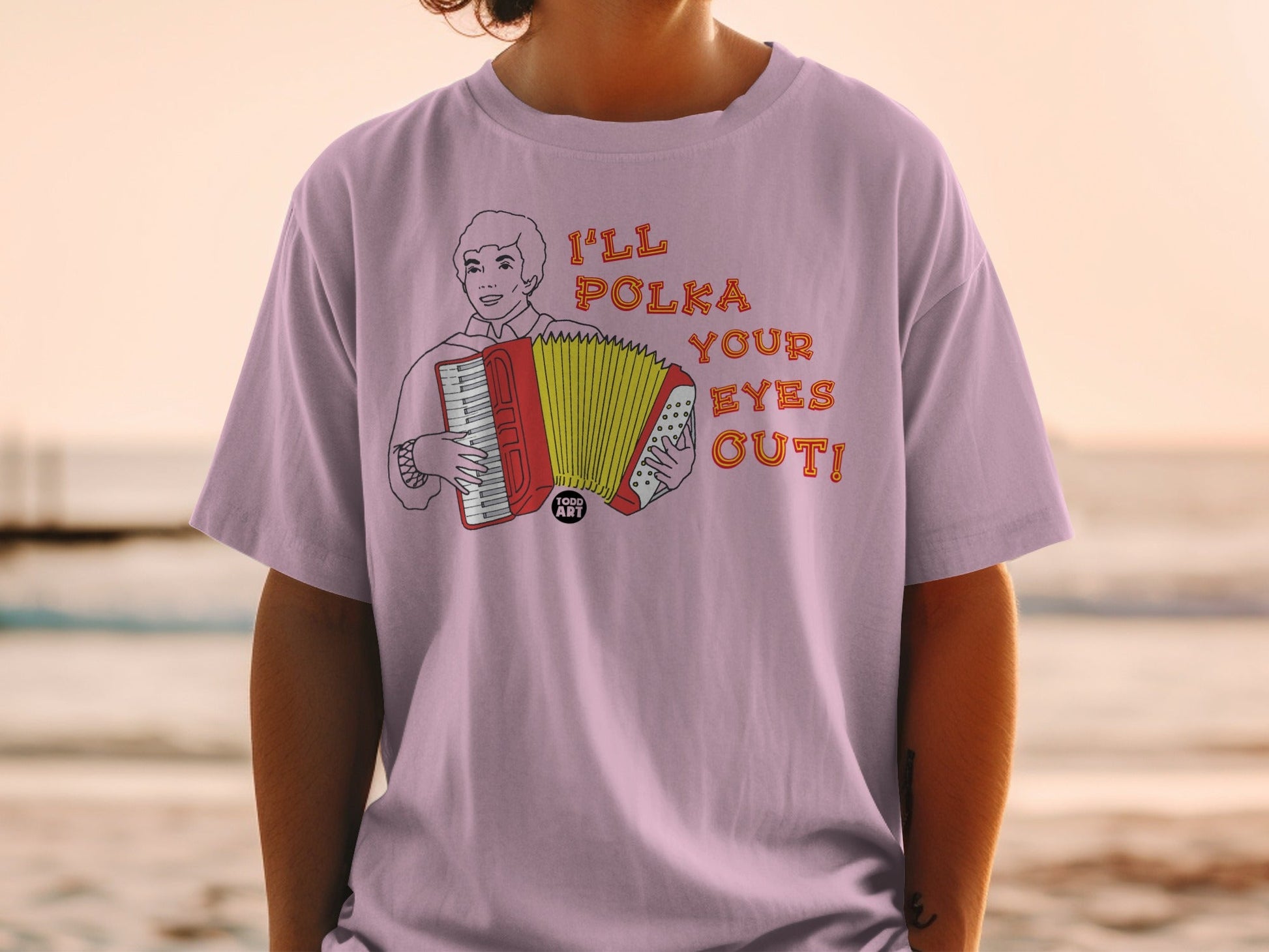 Pink t-shirt with a cartoon man playing an accordion and text "I'LL POLKA YOUR EYES OUT!"