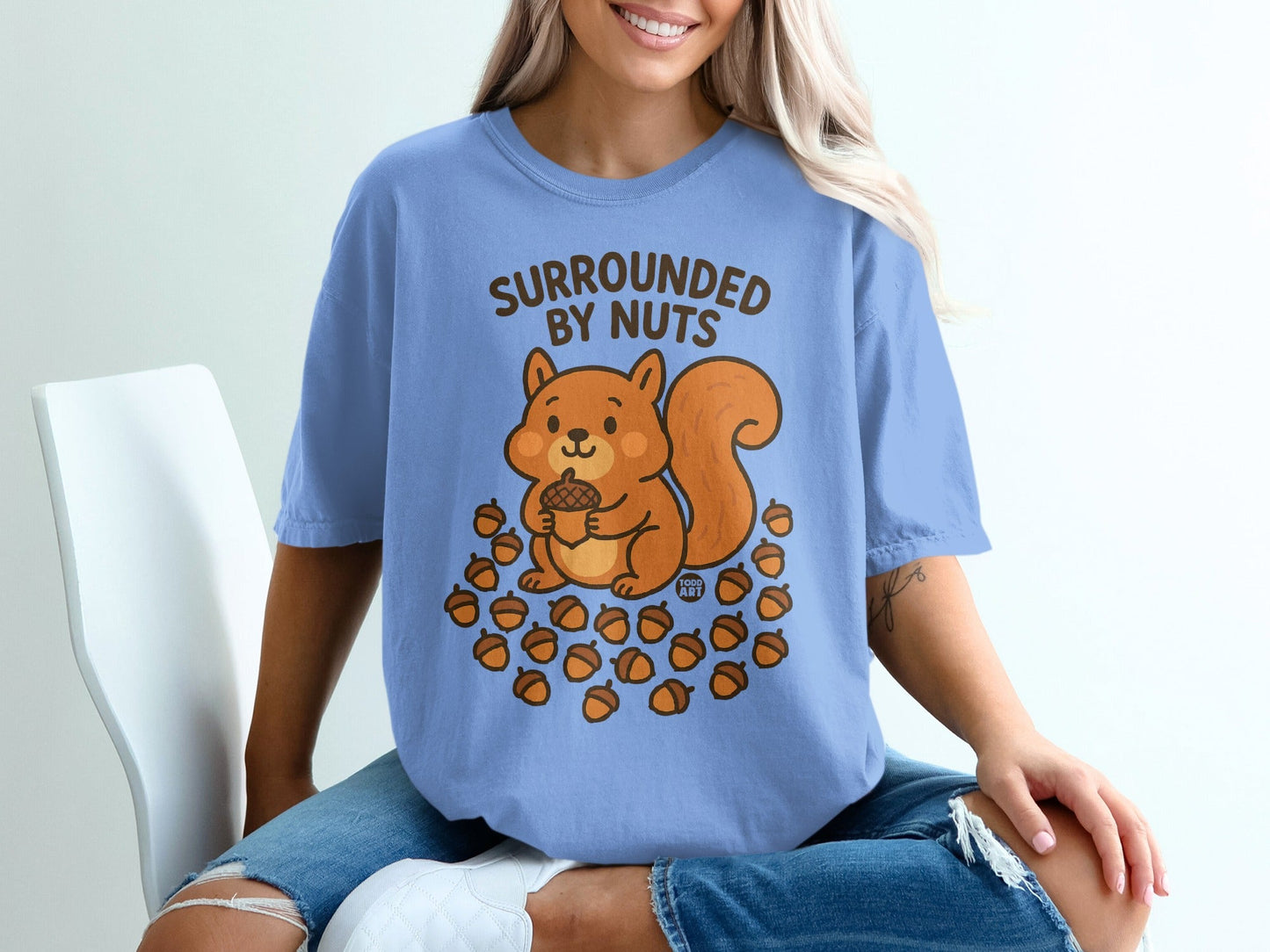 Light blue t-shirt with a cartoon squirrel and acorns, text "SURROUNDED BY NUTS".
