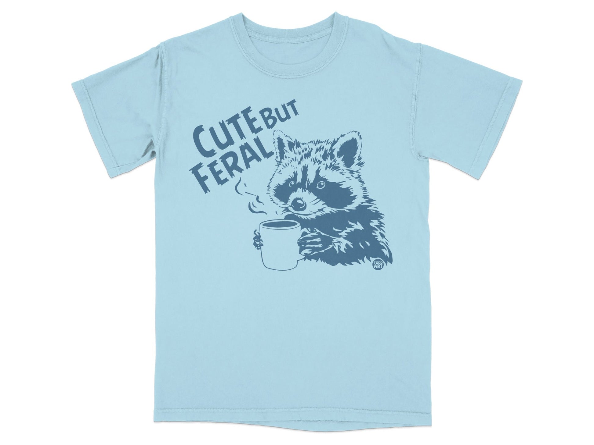 Light blue t-shirt with raccoon holding coffee mug, text "CUTE BUT FERAL".