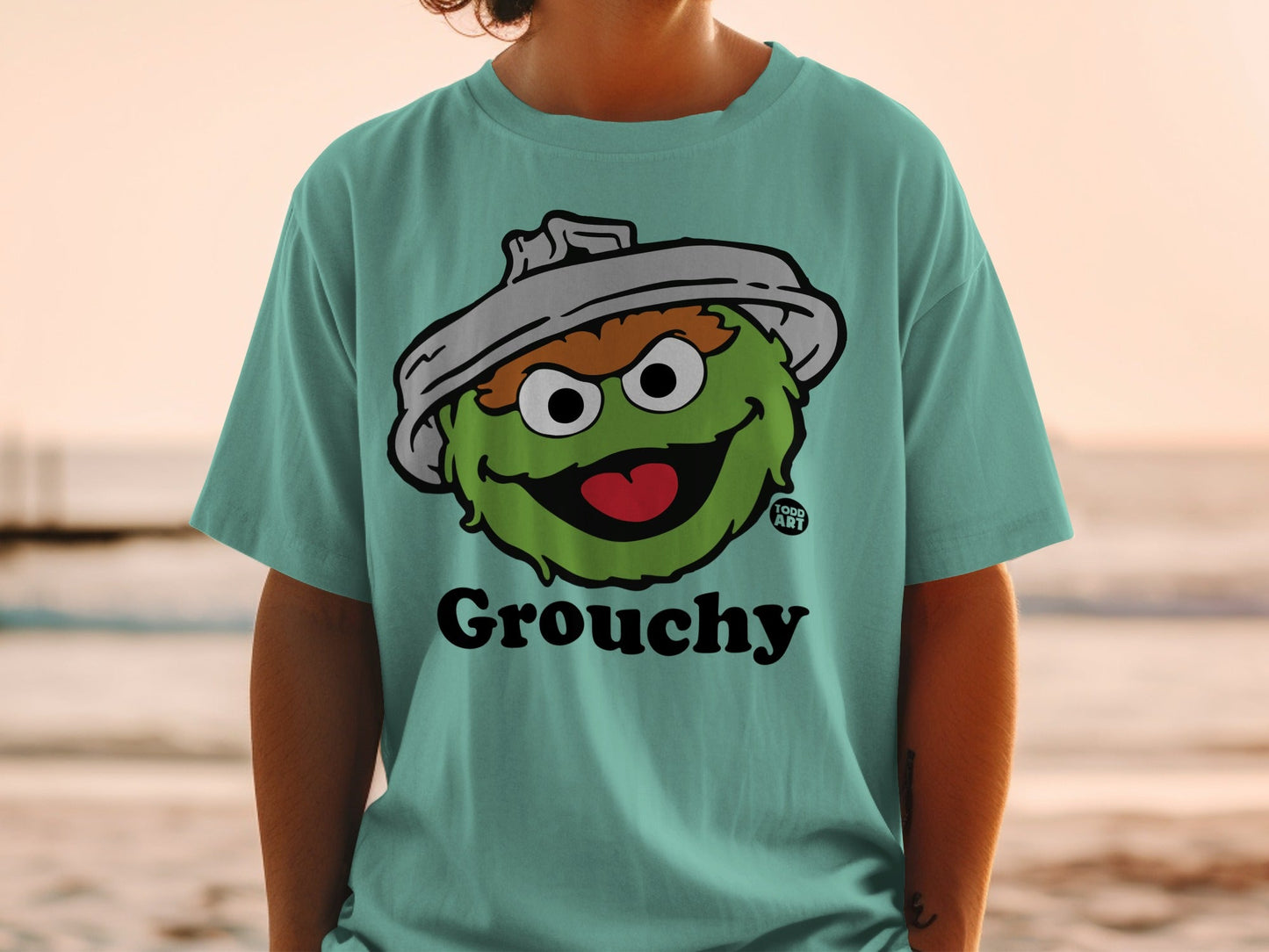 Green monster character wearing a shirt with "Grouchy" text and 1000 ANT logo.