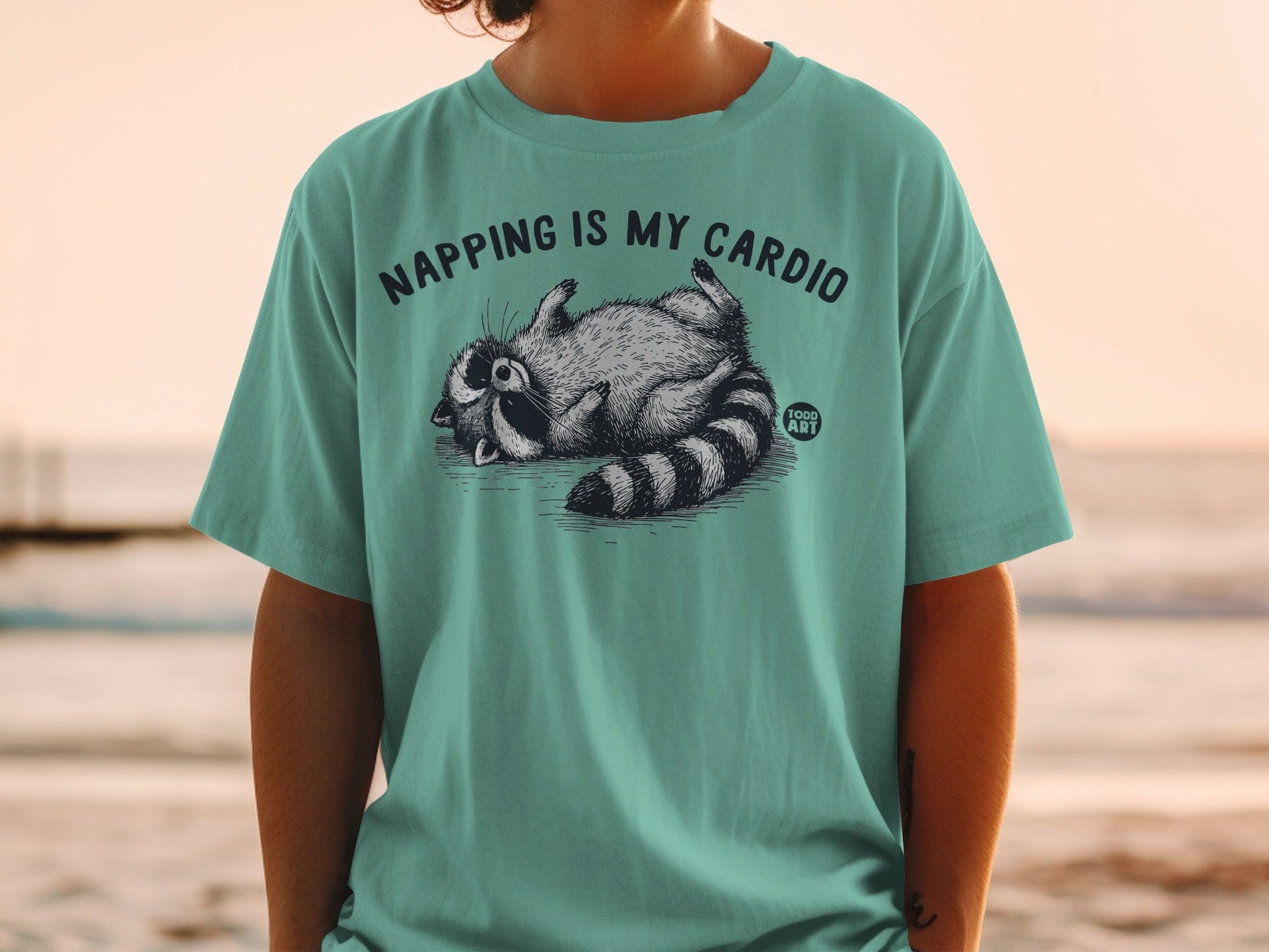 T-shirt with raccoon napping and text "NAPPING IS MY CARDIO".