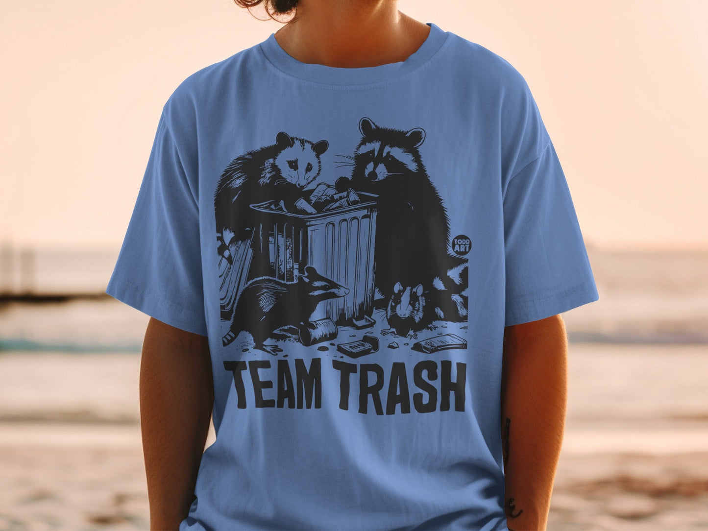 Blue t-shirt with "TEAM TRASH" text and raccoons and opossum rummaging in a trash can.
