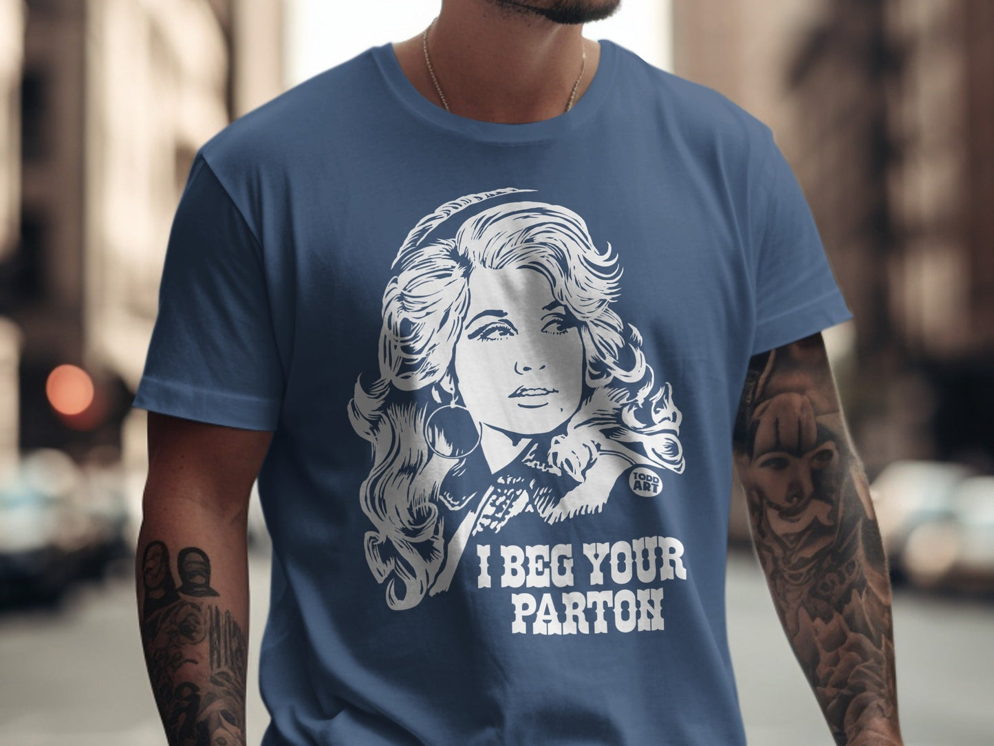 Blue t-shirt with white graphic of Dolly Parton and text "I BEG YOUR PARTON".
