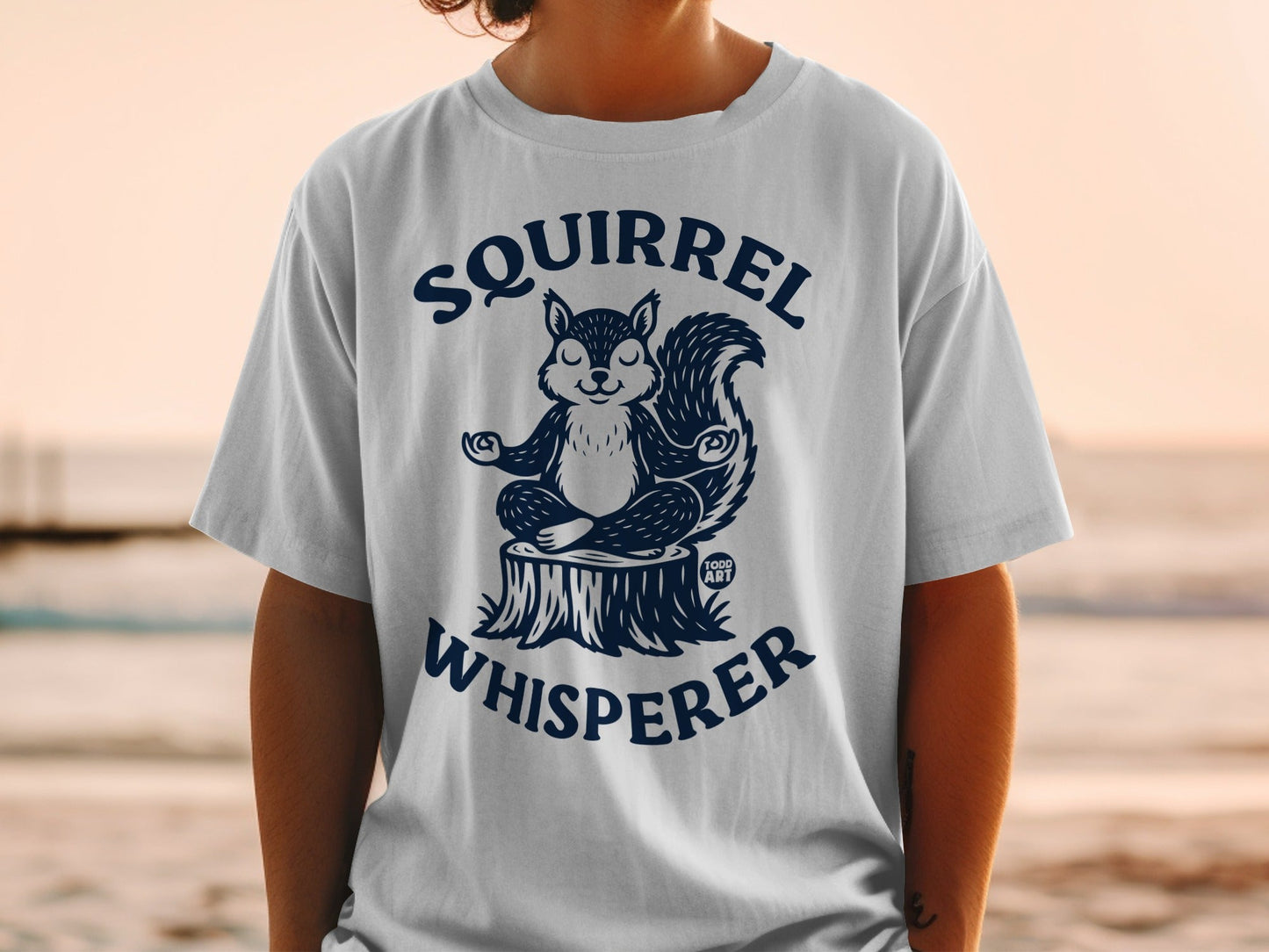 White t-shirt with navy graphic of meditating squirrel, "Squirrel Whisperer" text.