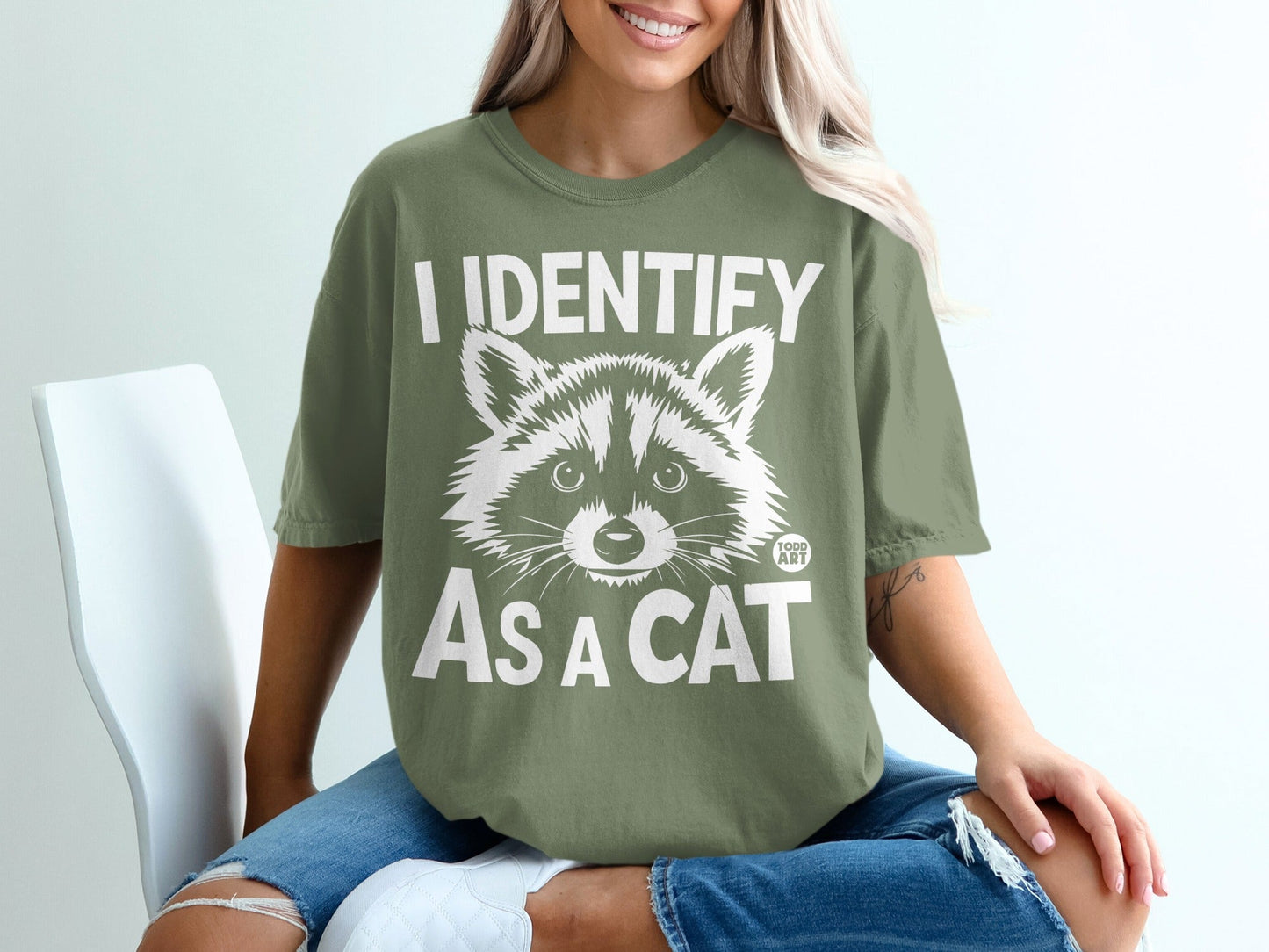 Olive green t-shirt with "I IDENTIFY AS A CAT" and raccoon graphic.