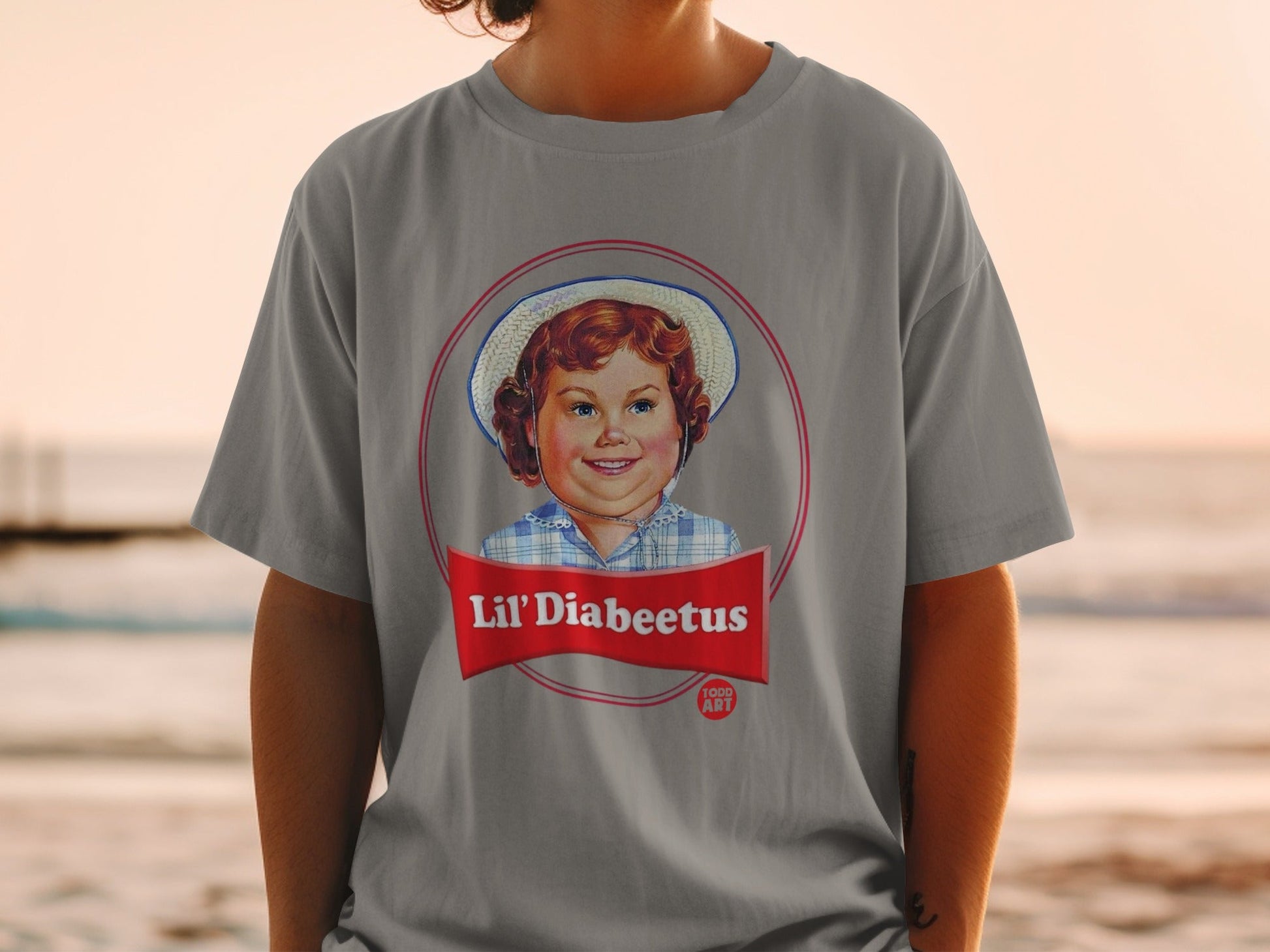 Lil' Diabeetus logo featuring a smiling child in a hat on a grey t-shirt.