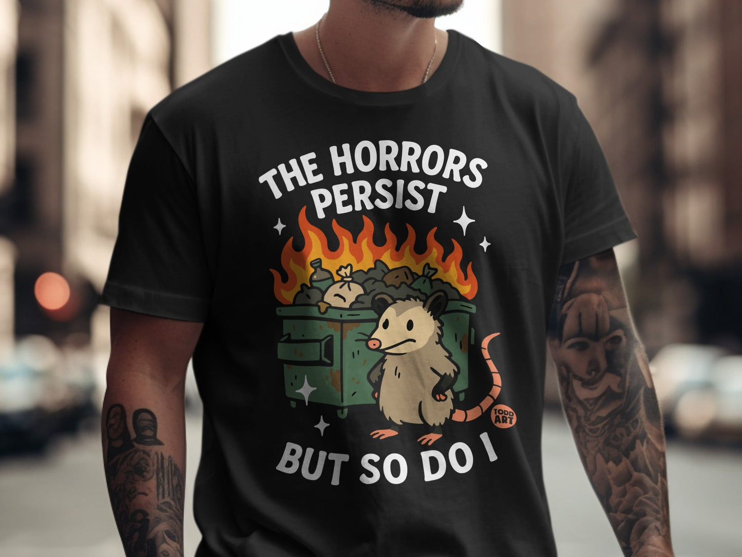 Black t-shirt with "The Horrors Persist But So Do I" text and cartoon possum in flames.