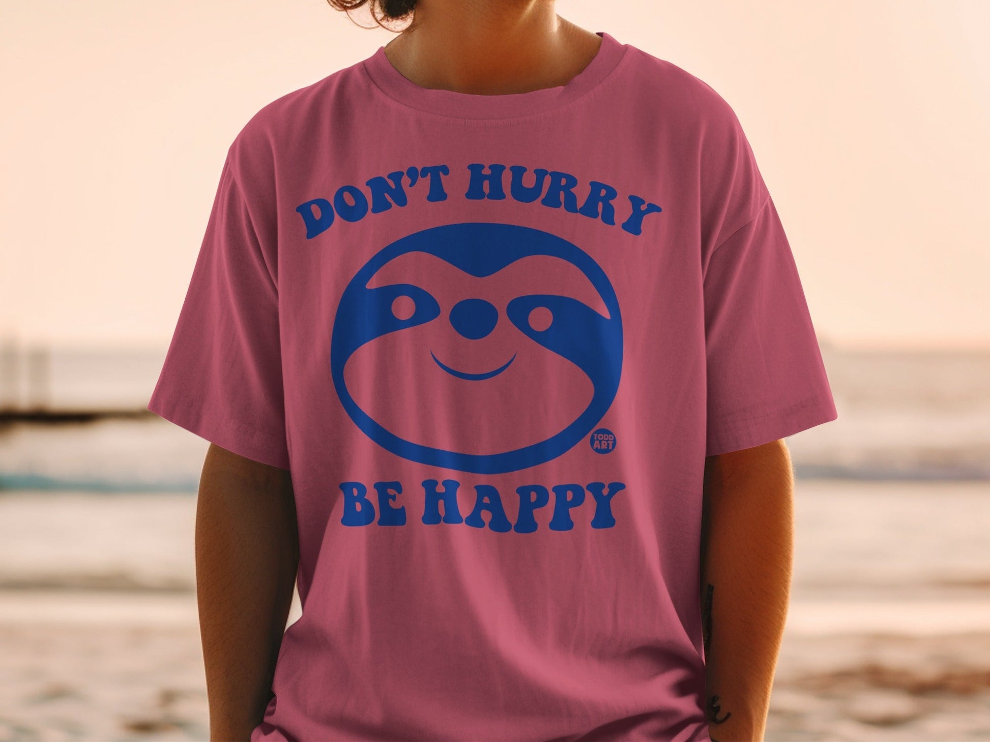 Pink t-shirt with a blue sloth graphic and "DON'T HURRY BE HAPPY" text.