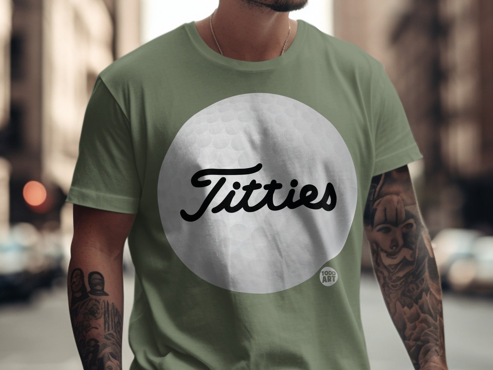 Green t-shirt with "Titties" in cursive on a golf ball graphic.