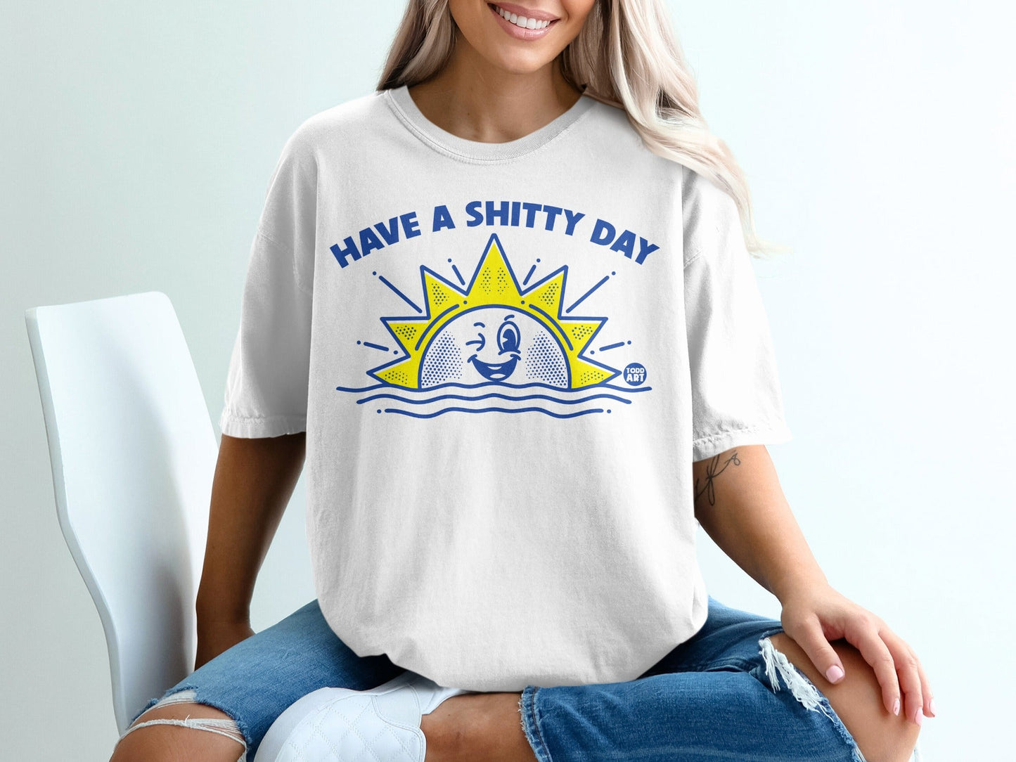 White t-shirt with blue sun graphic saying "HAVE A SHITTY DAY".