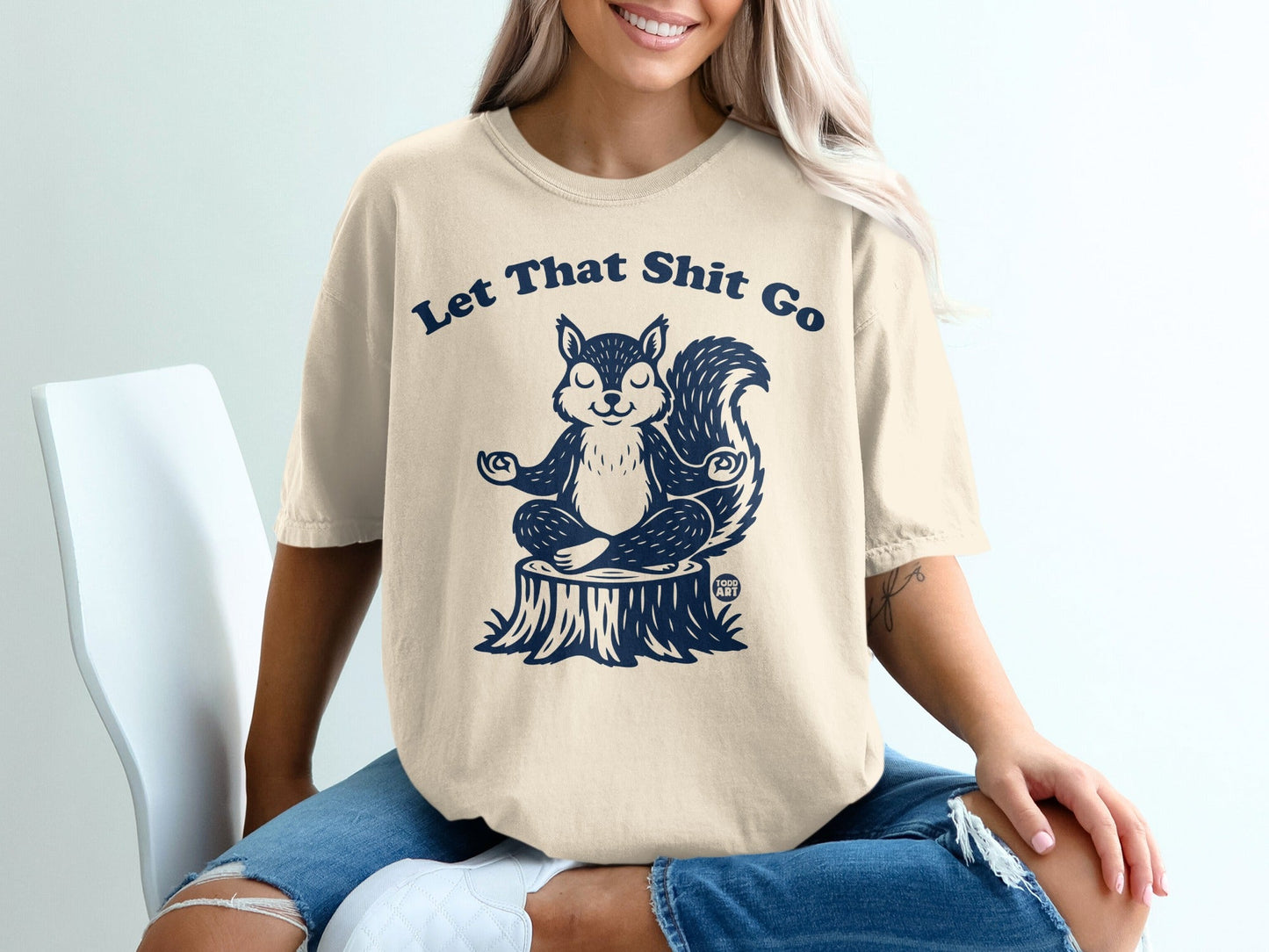 Cream t-shirt with a meditating squirrel graphic and "Let That Shit Go" text.