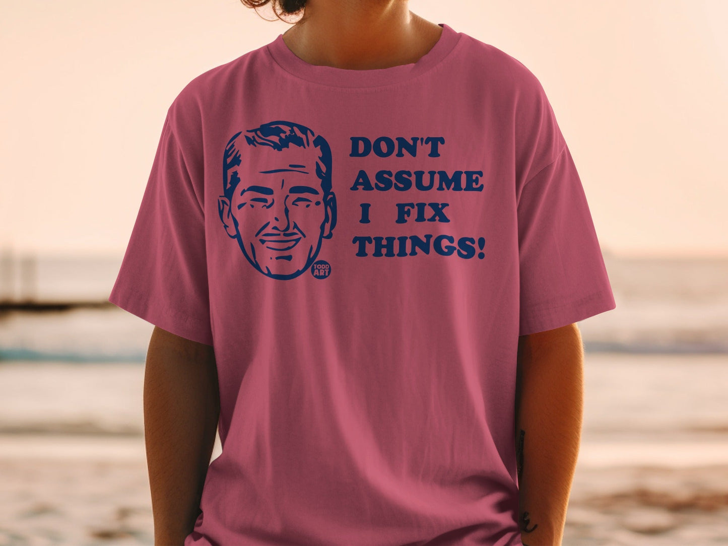 Pink t-shirt with man's face and "Don't assume I fix things!" text.
