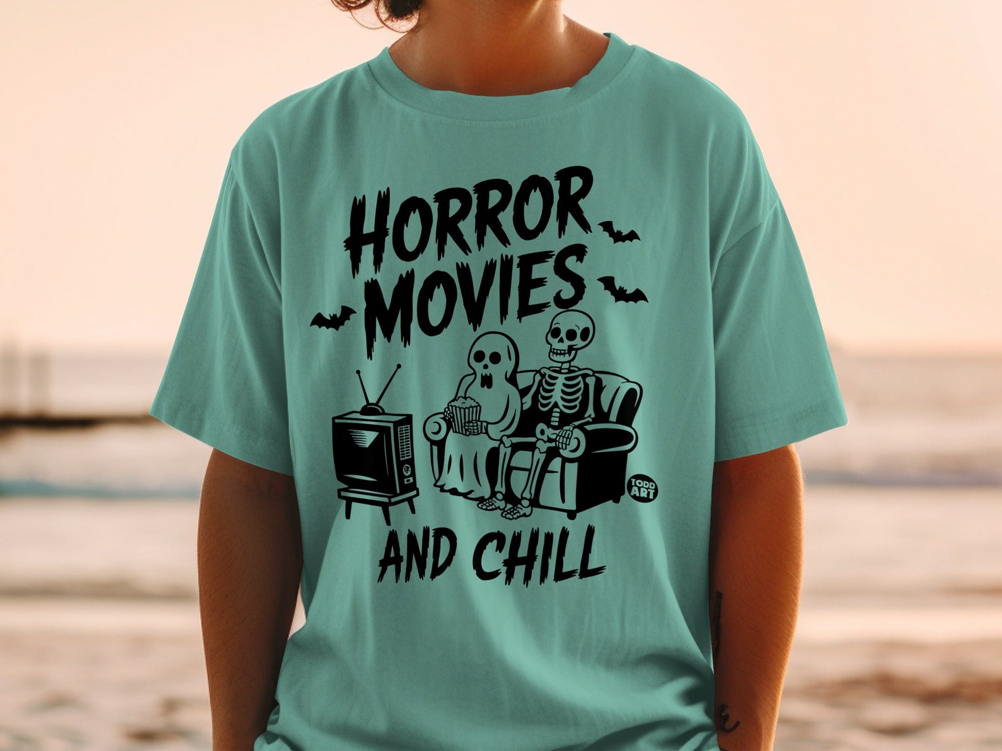 Skeleton couple watching horror movies and eating popcorn on teal t-shirt.