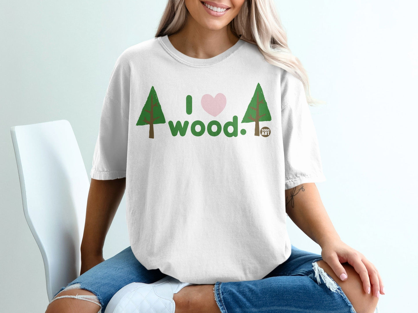 White t-shirt with green trees and pink heart, "I love wood." text.