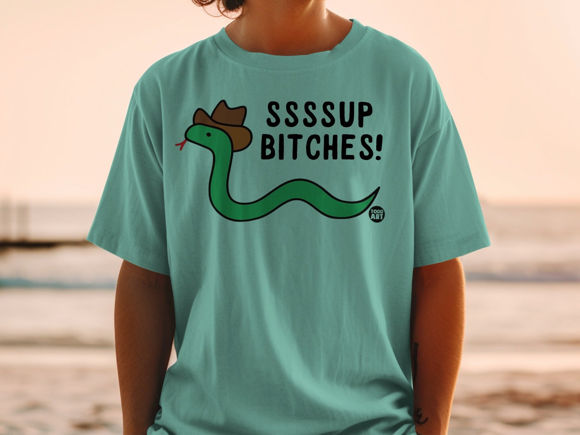 Green cartoon snake wearing a cowboy hat and the text "SSSUP BITCHES!" on a t-shirt.