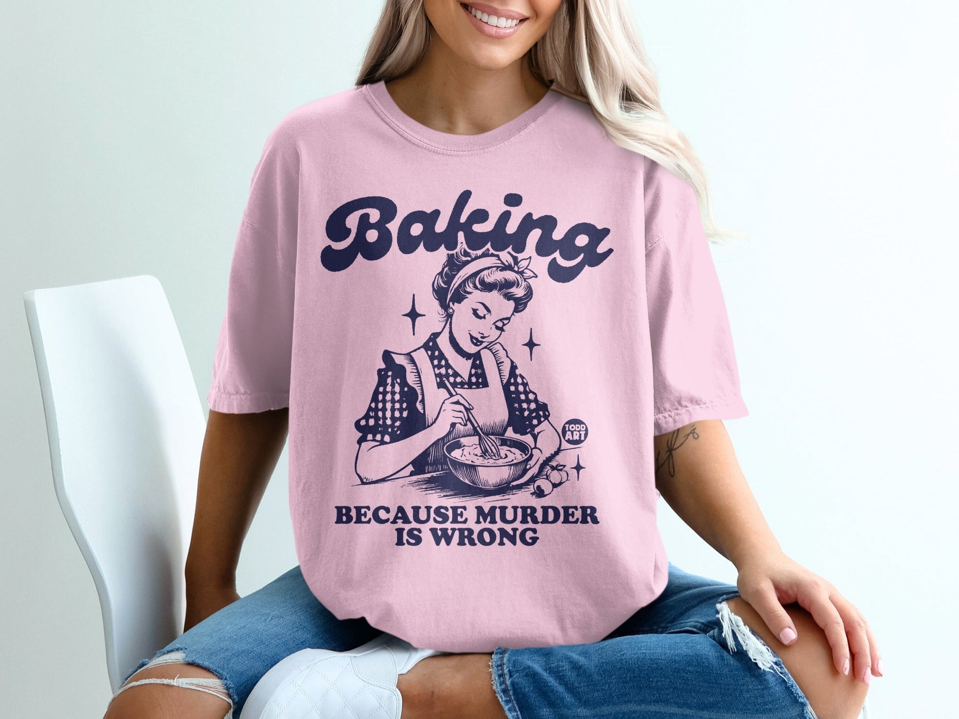 Pink t-shirt with "Baking Because Murder Is Wrong" text and retro baking graphic.