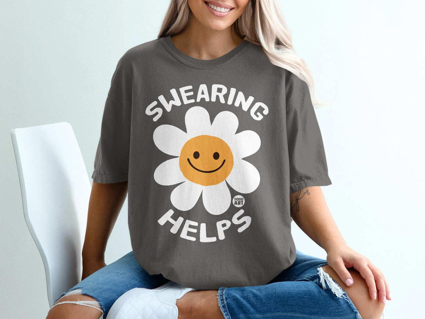 Grey t-shirt with a smiling daisy and text "SWEARING HELPS".