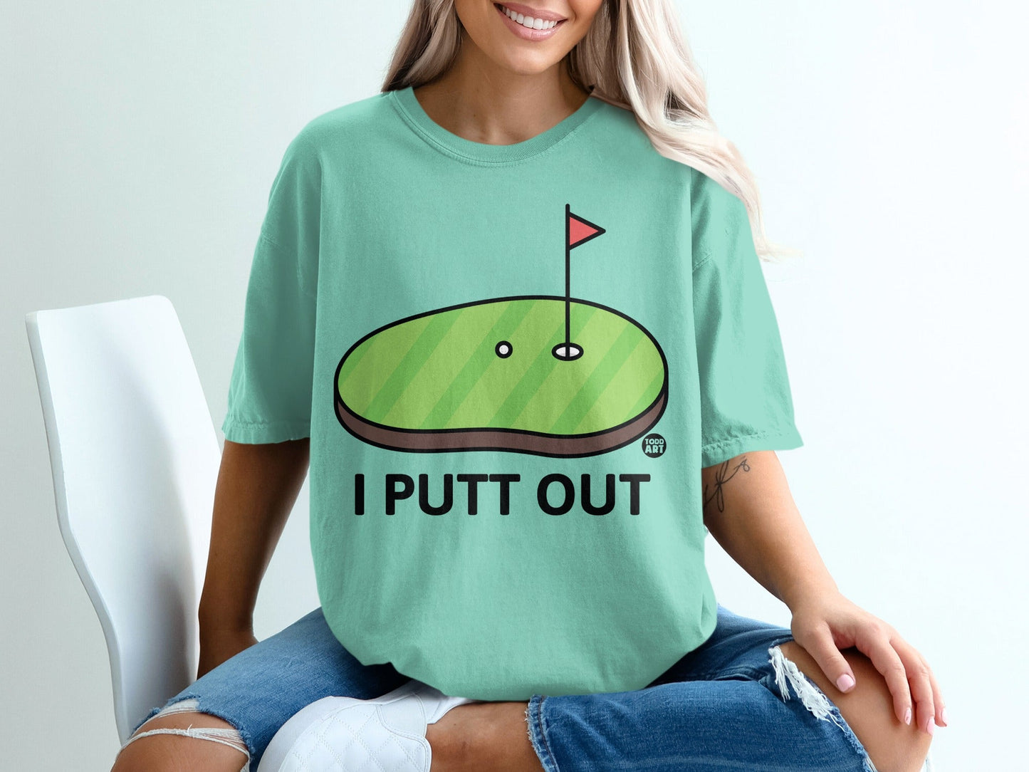 Teal t-shirt with cartoon golf putting green and text "I PUTT OUT".