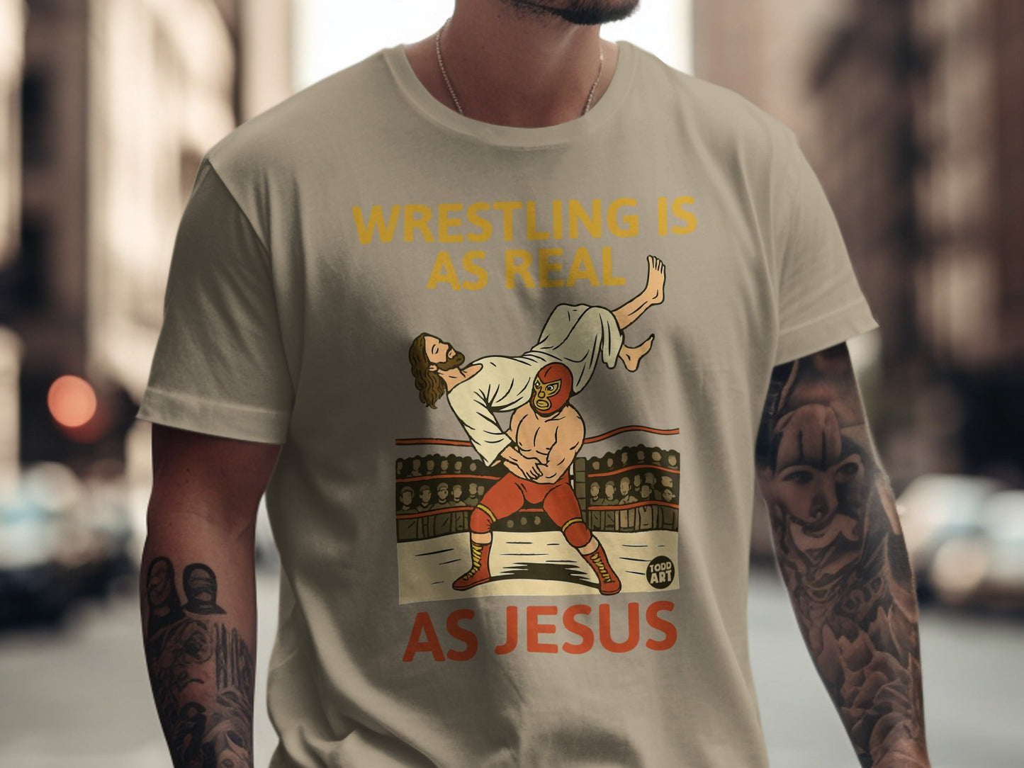 T-shirt graphic: wrestler body slams Jesus in a ring with text "Wrestling is real as Jesus".