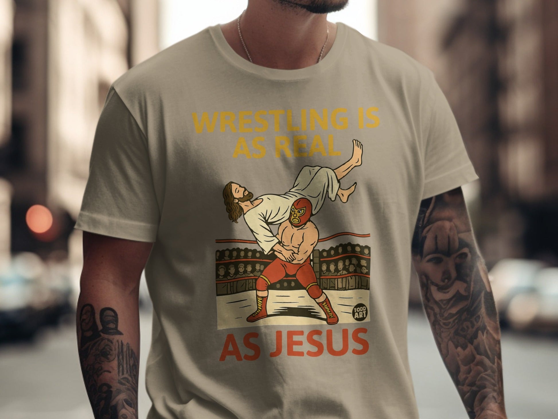 T-shirt graphic: wrestler body slams Jesus in a ring with text "Wrestling is real as Jesus".