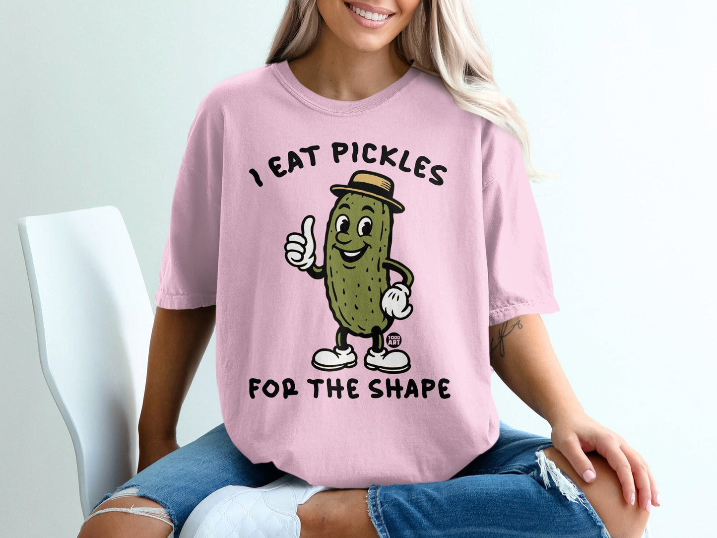 Pink t-shirt with pickle character saying "I eat pickles for the shape."
