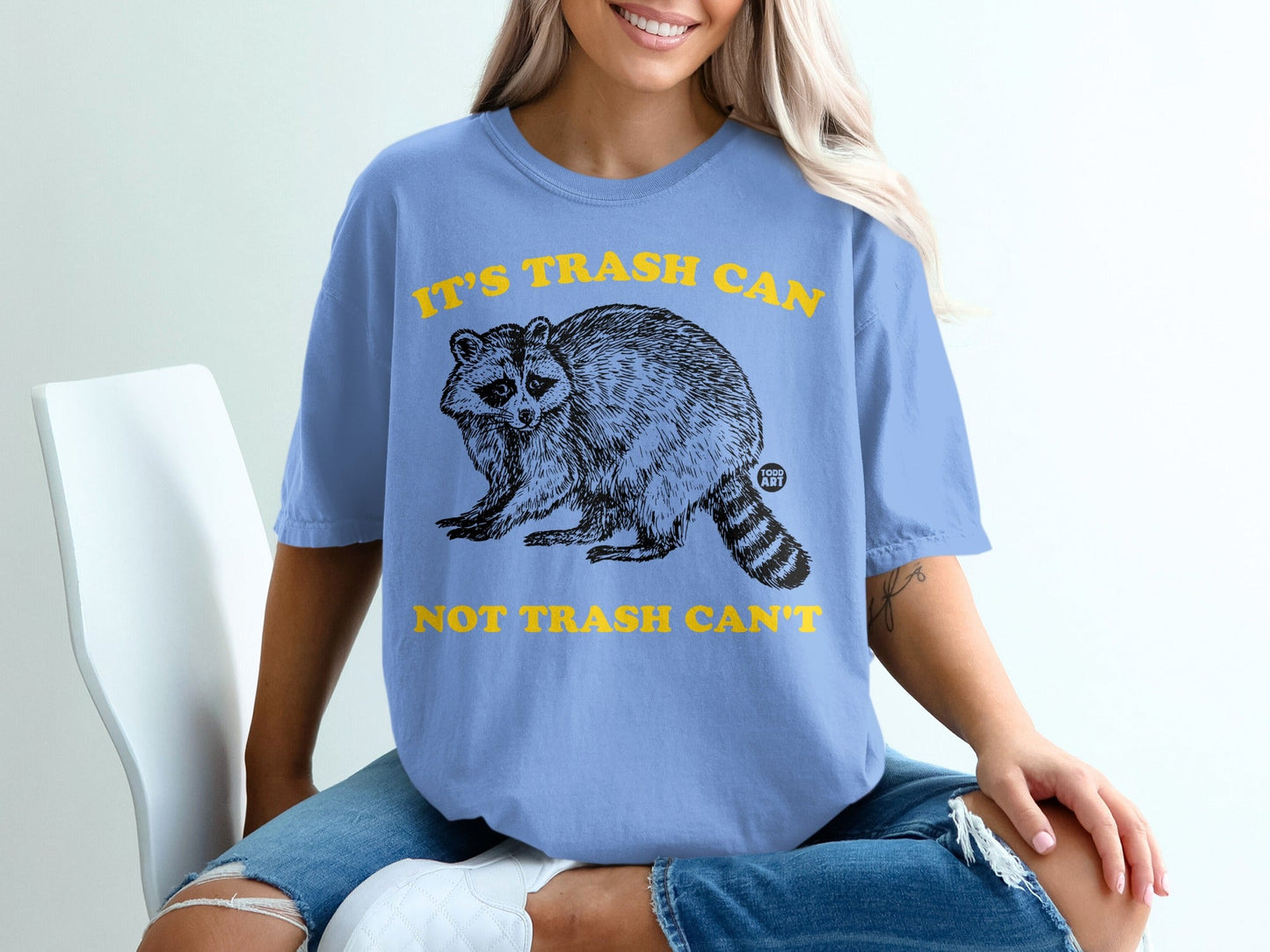 Blue t-shirt with raccoon graphic and yellow text: "IT'S TRASH CAN NOT TRASH CAN'T".