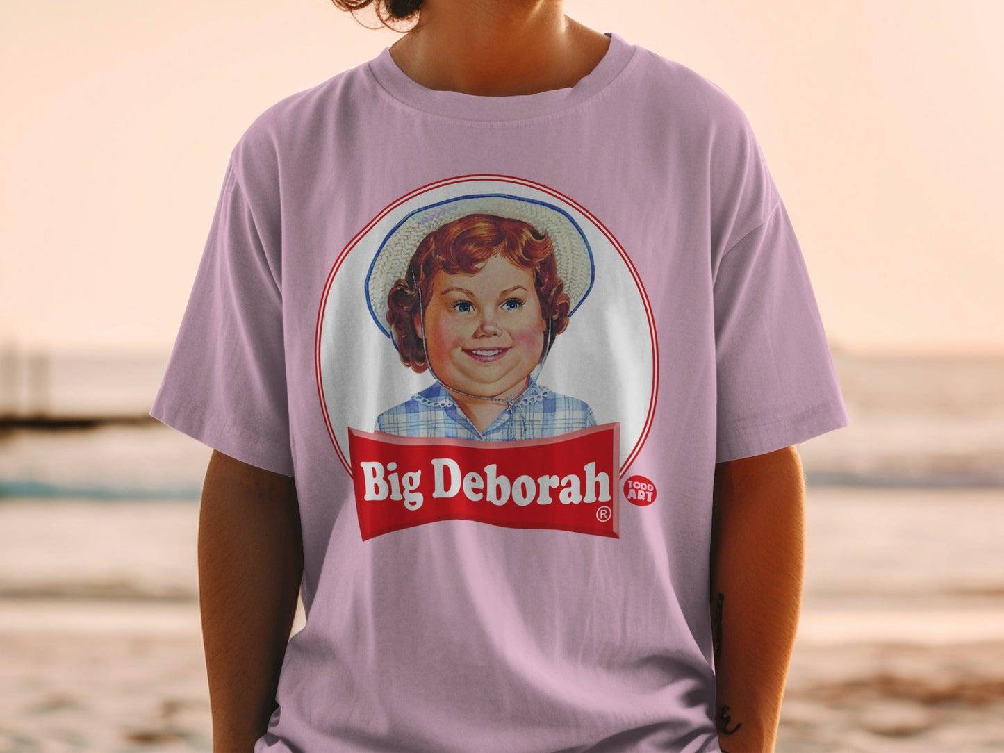 Pink t-shirt with a circular logo featuring a young girl and "Big Deborah" text.
