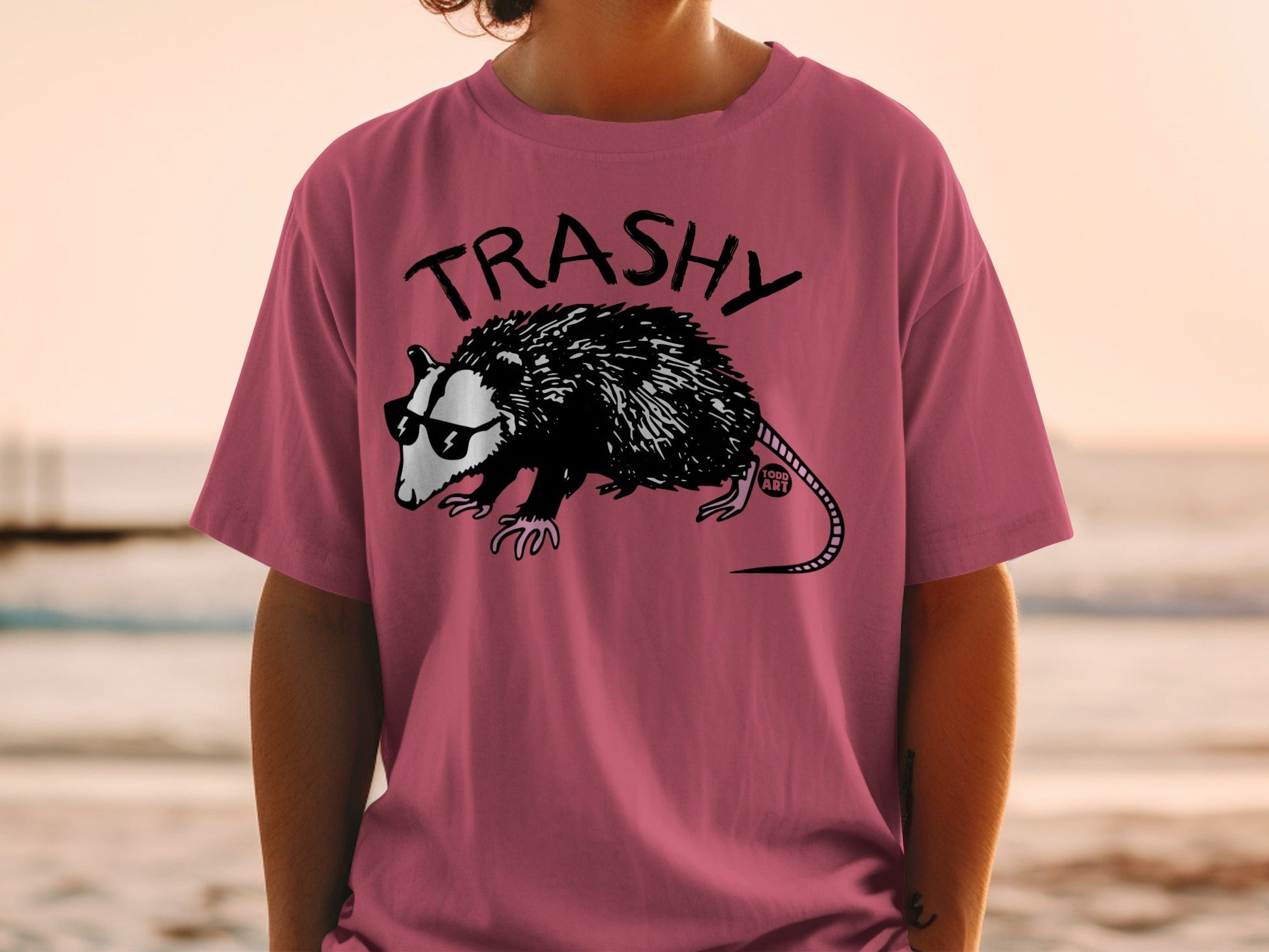 Pink t-shirt with a raccoon wearing sunglasses and the word "TRASHY".