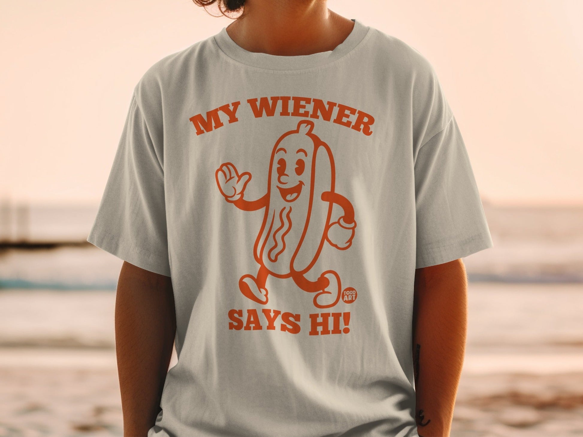 Orange t-shirt with a cartoon hot dog that says "My Wiener Says Hi!".