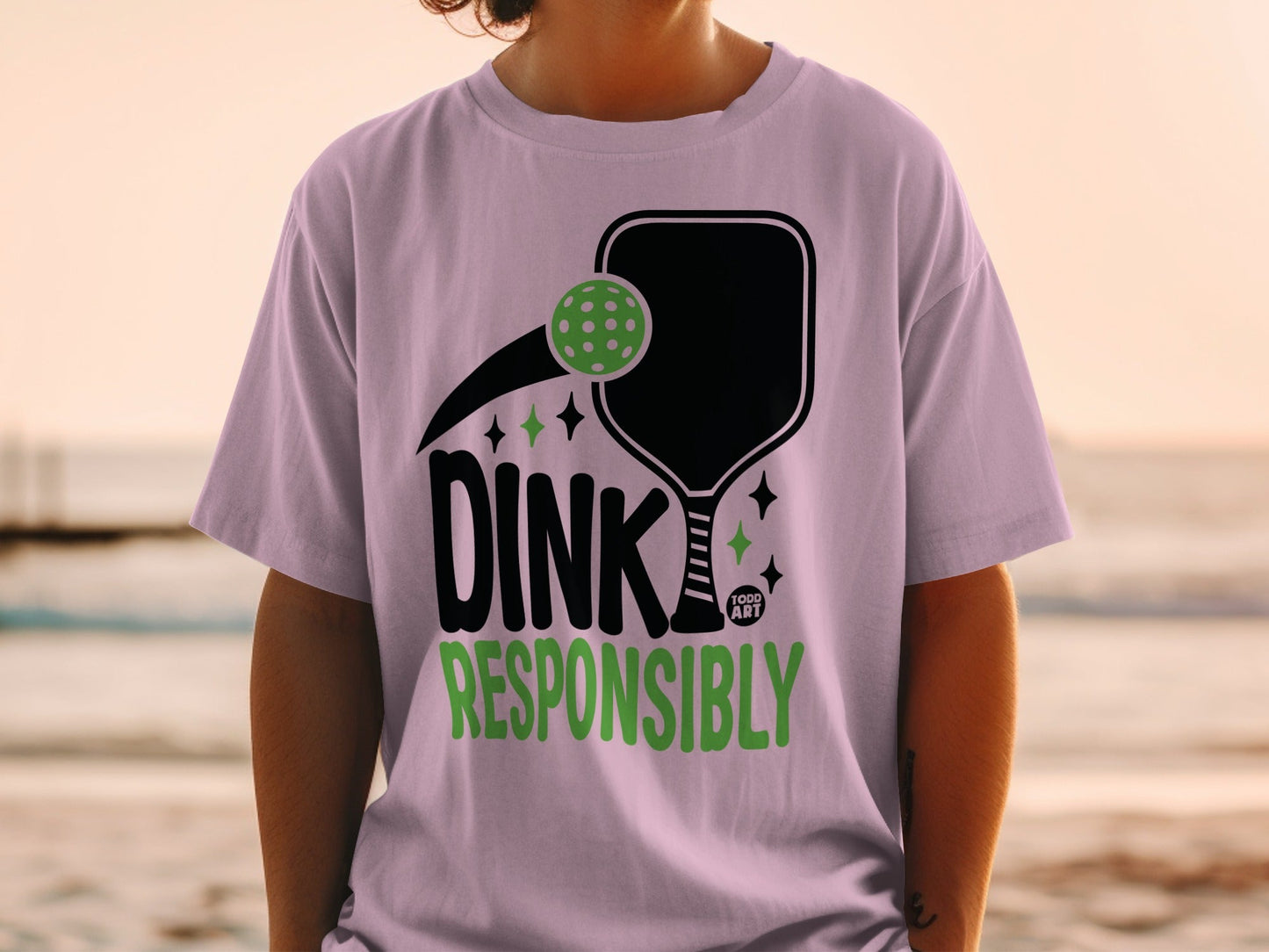 T-shirt with black pickleball paddle and green ball, "DINK RESPONSIBLY" text.