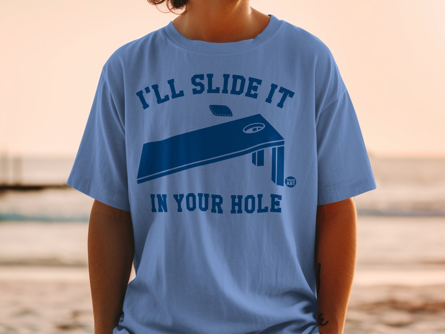 Blue t-shirt with cornhole board graphic and text.