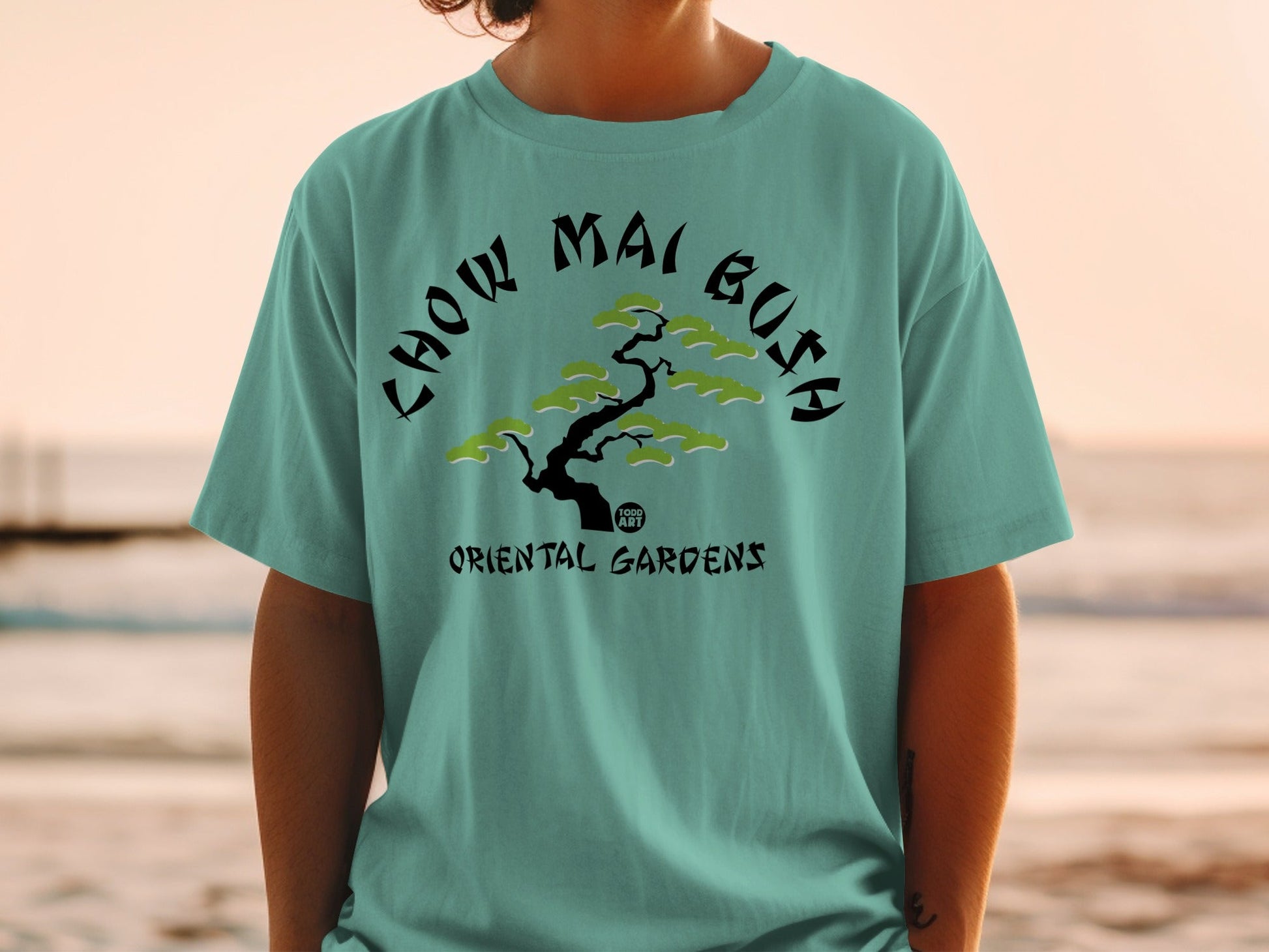Teal t-shirt with black text and a stylized green tree graphic.