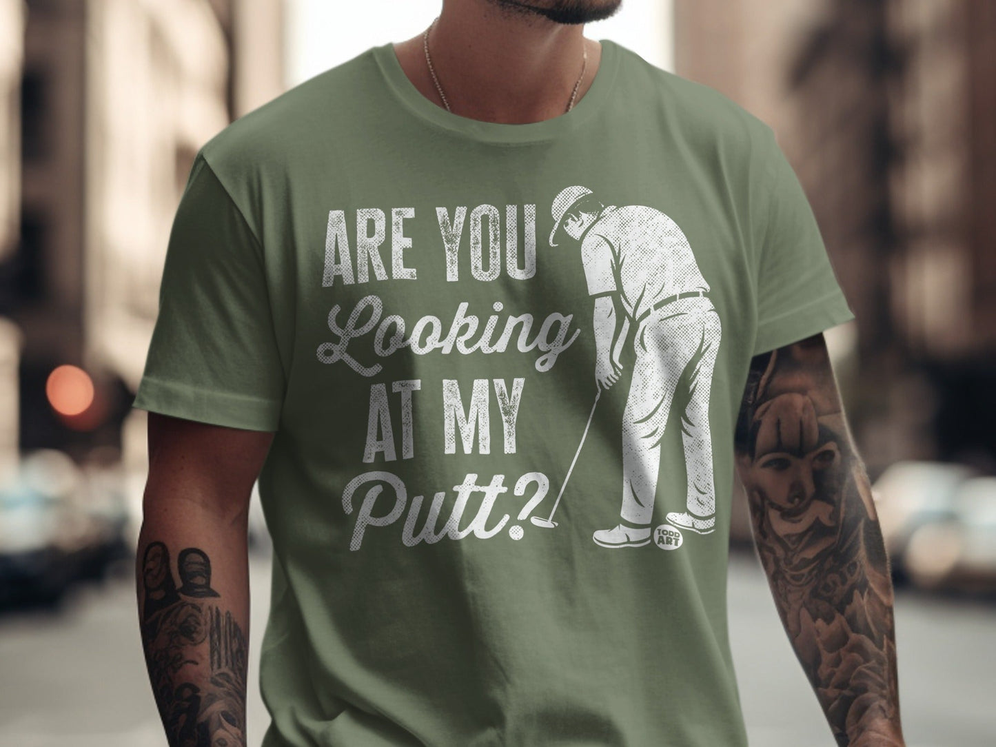 Olive green t-shirt with "ARE YOU LOOKING AT MY PUTT?" and golfer graphic.