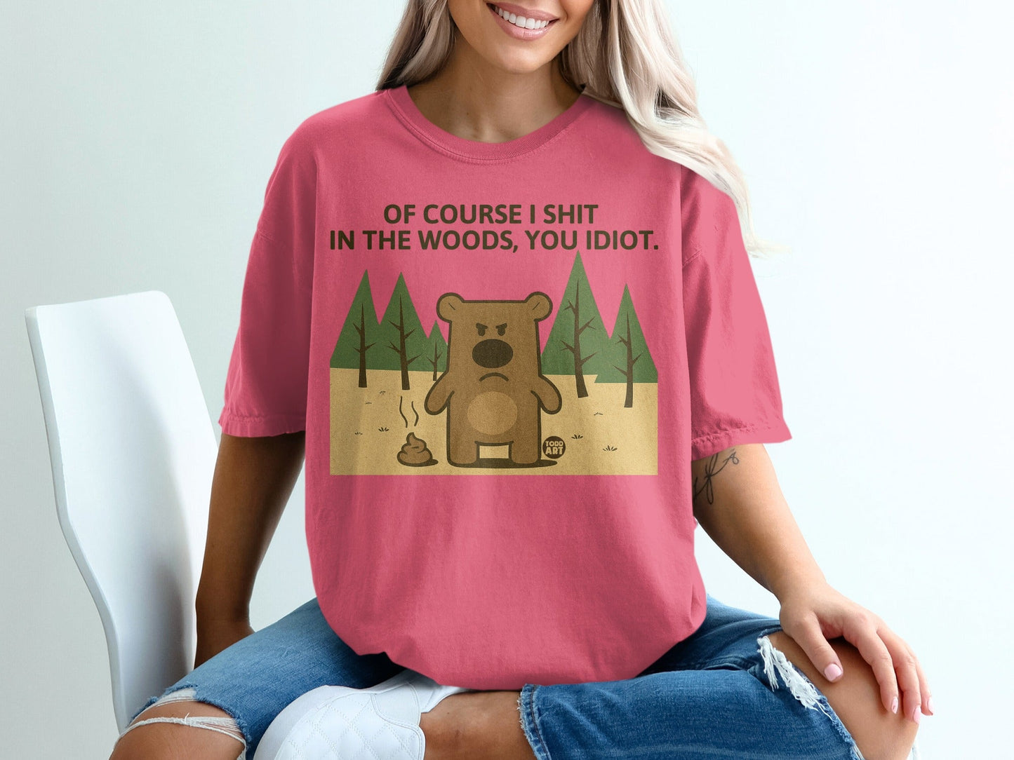 Pink t-shirt with cartoon bear, trees, and text "OF COURSE I SHIT IN THE WOODS, YOU IDIOT."