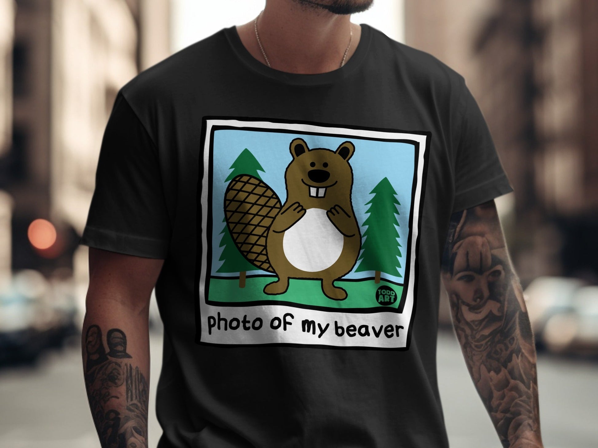 T-shirt with cartoon beaver illustration in blue sky and green trees.