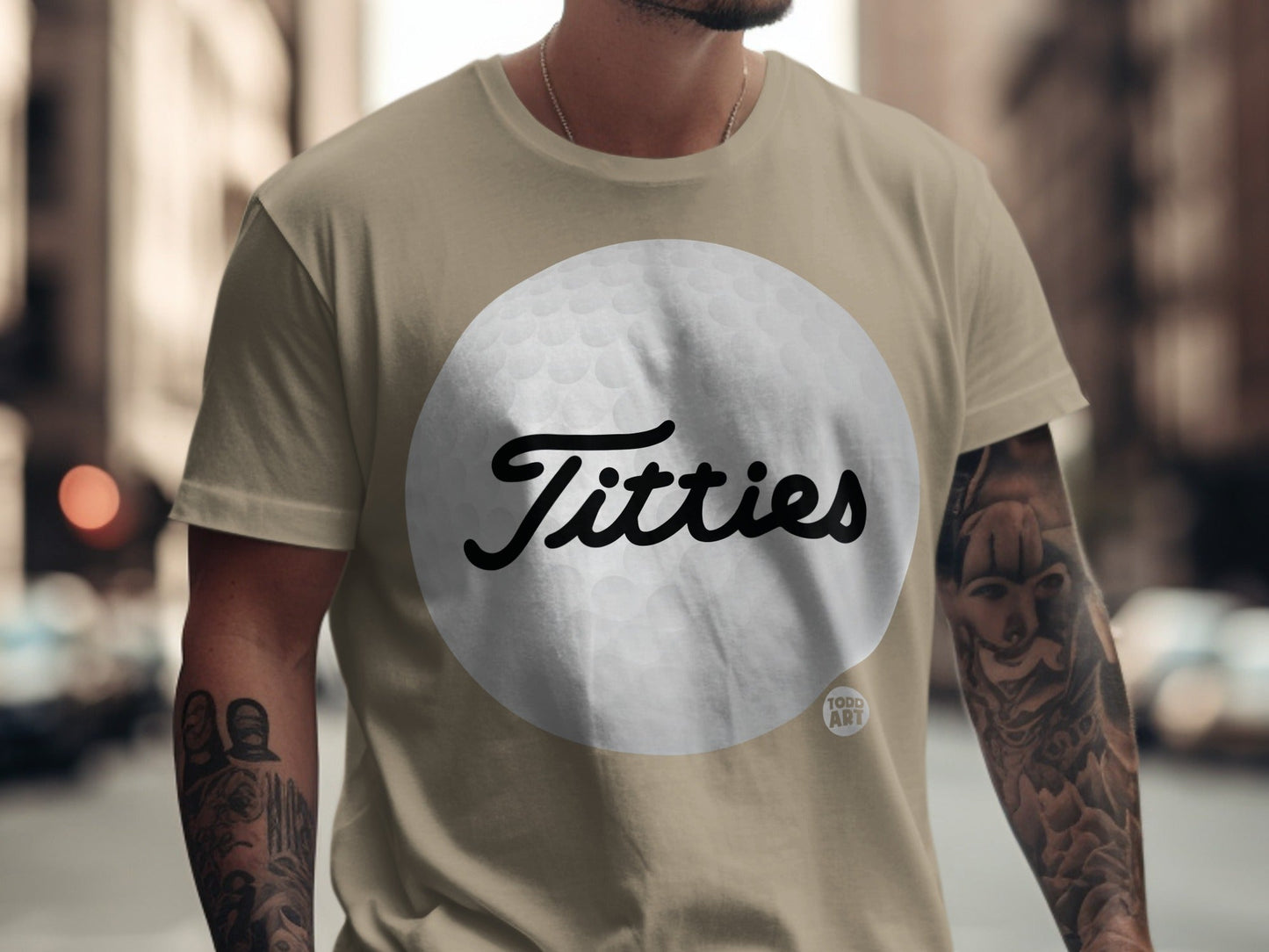 Tan t-shirt with a gray golf ball graphic and the word "Titties".