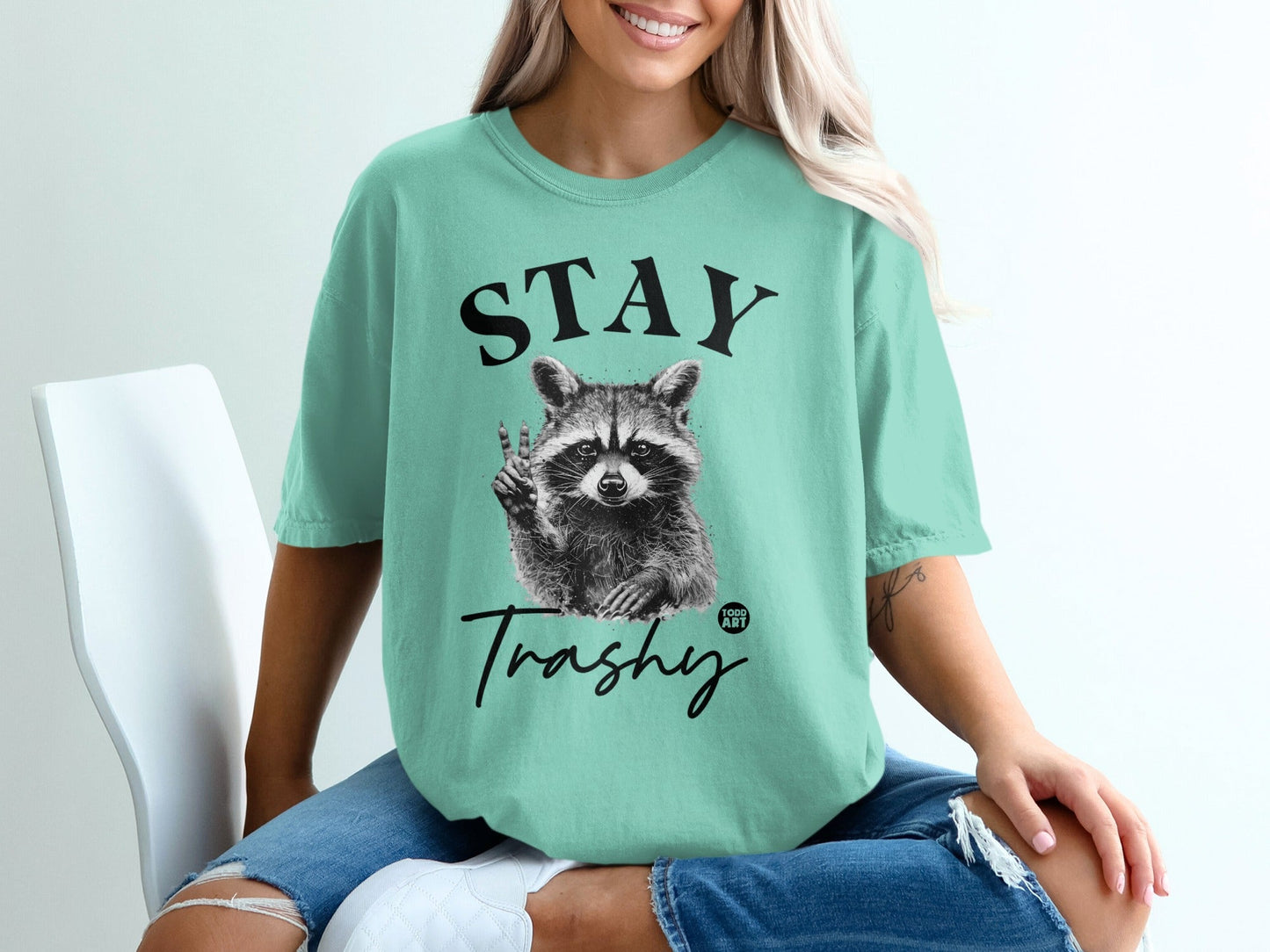 Teal t-shirt with raccoon giving peace sign and "STAY Trashy" text.