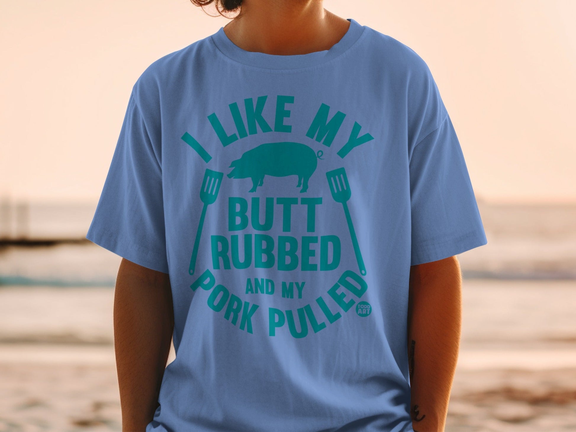 Blue t-shirt with teal text "I like my butt rubbed and pork pulled" and pig silhouette.