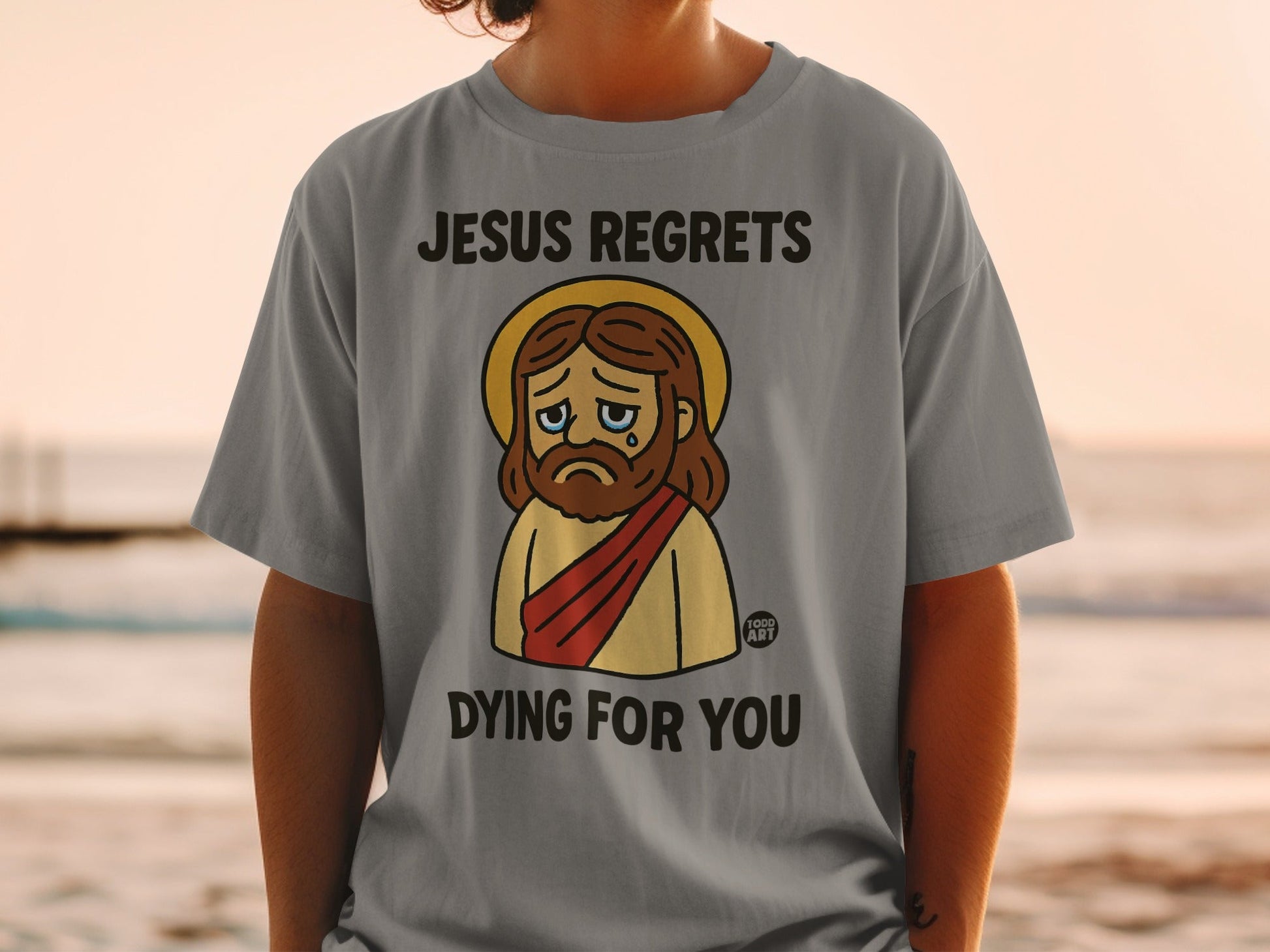 Jesus cartoon on t-shirt with text "JESUS REGRETS DYING FOR YOU".