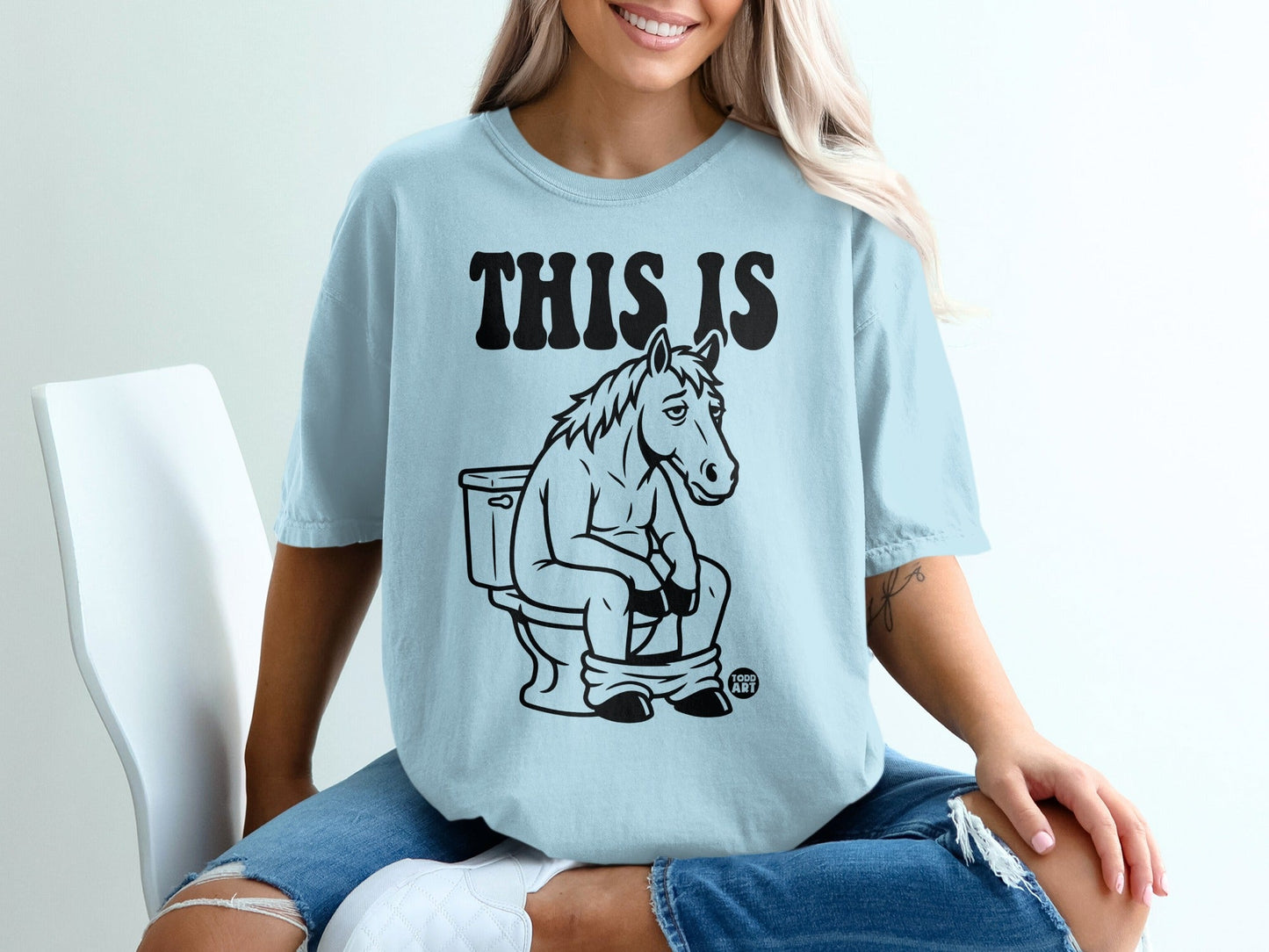 Light blue t-shirt with a cartoon horse sitting on a toilet.