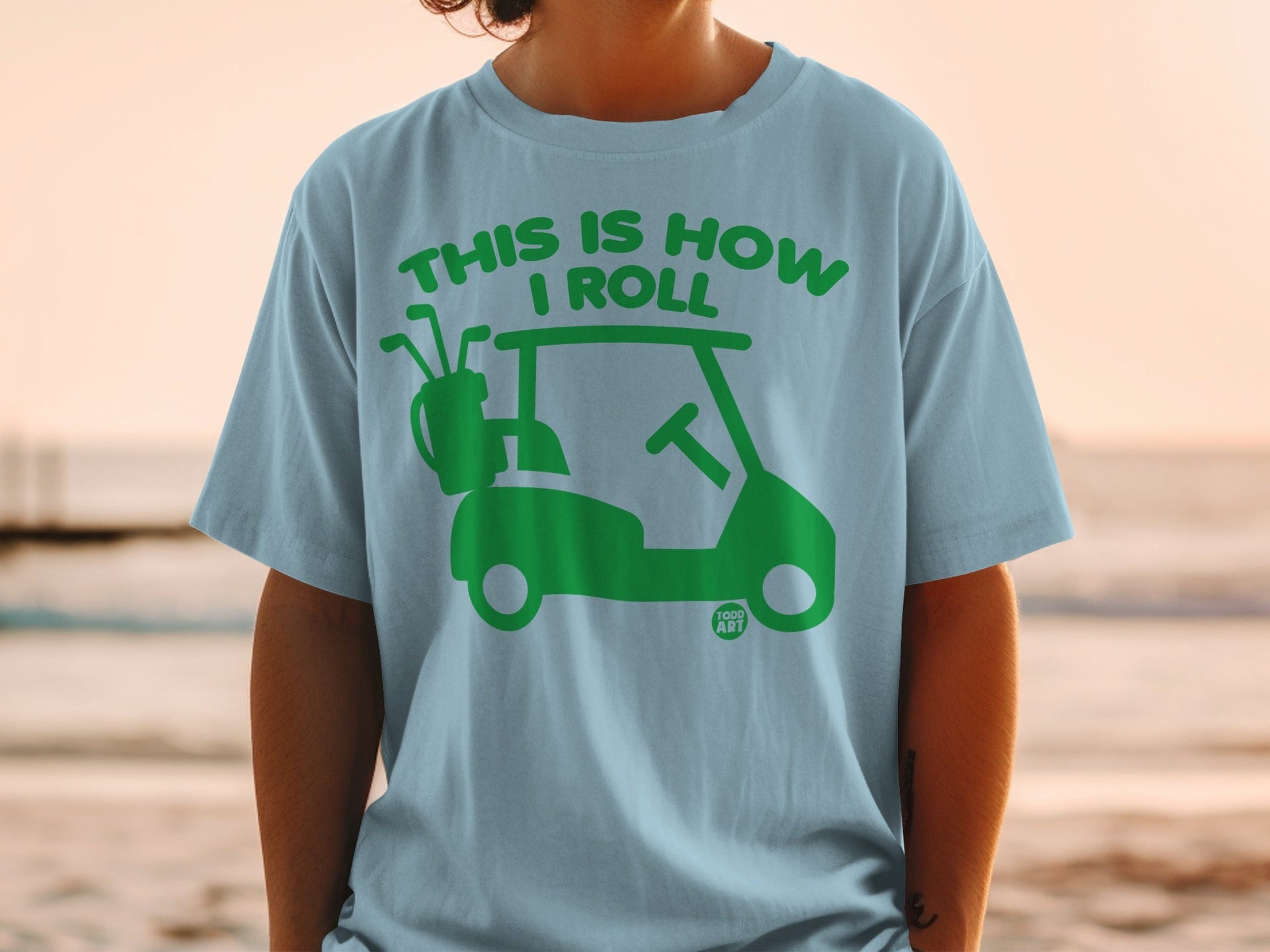Light blue t-shirt with green golf cart graphic and text "THIS IS HOW I ROLL".