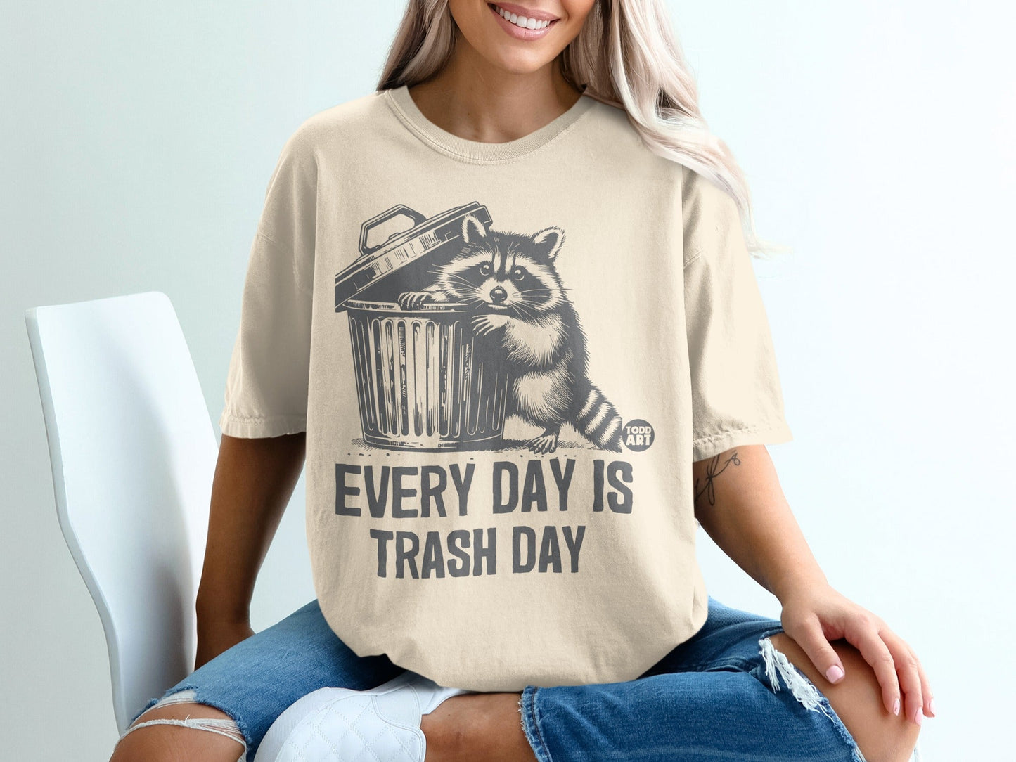 T-shirt with a raccoon peeking out of a trash can, text "EVERY DAY IS TRASH DAY".