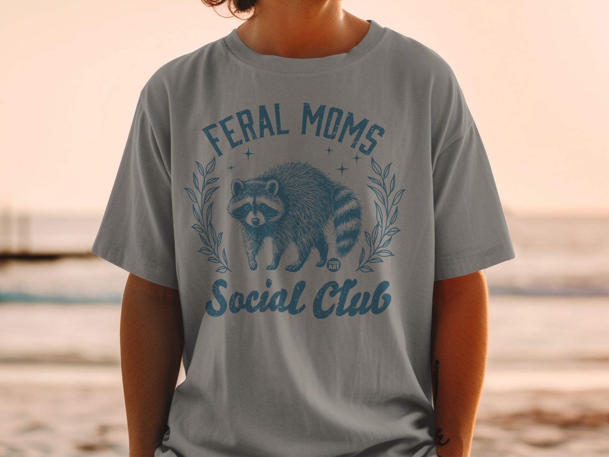 Grey t-shirt with raccoon and text "Feral Moms Social Club".