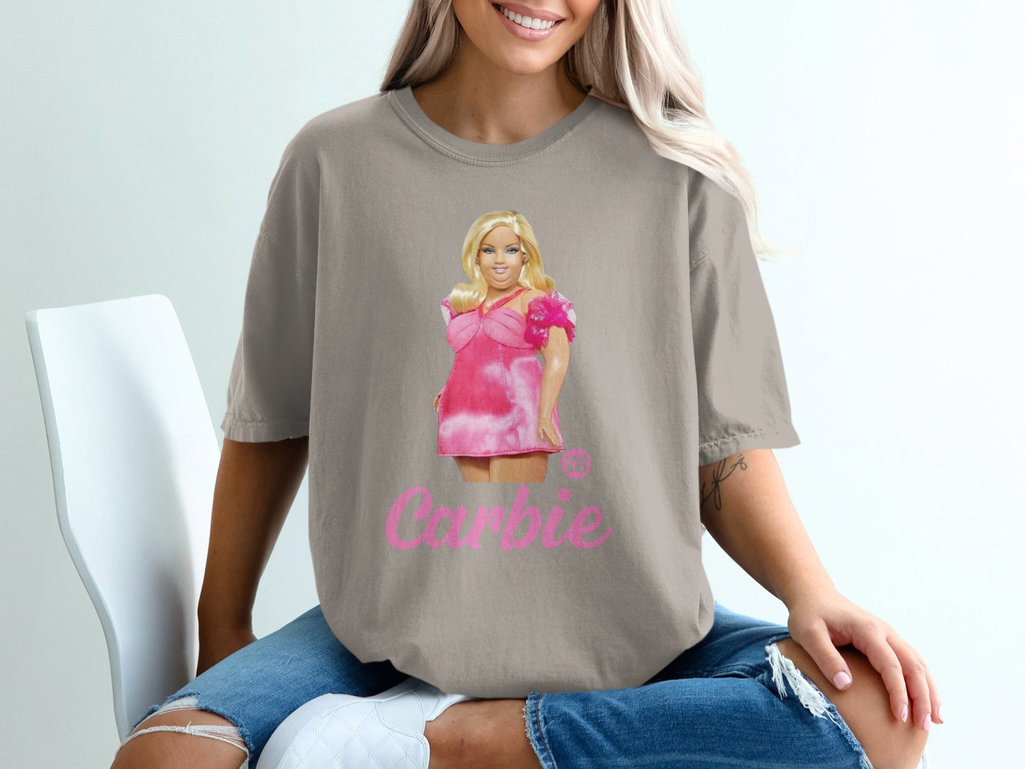 Woman wearing tan t-shirt with Barbie graphic and pink text.