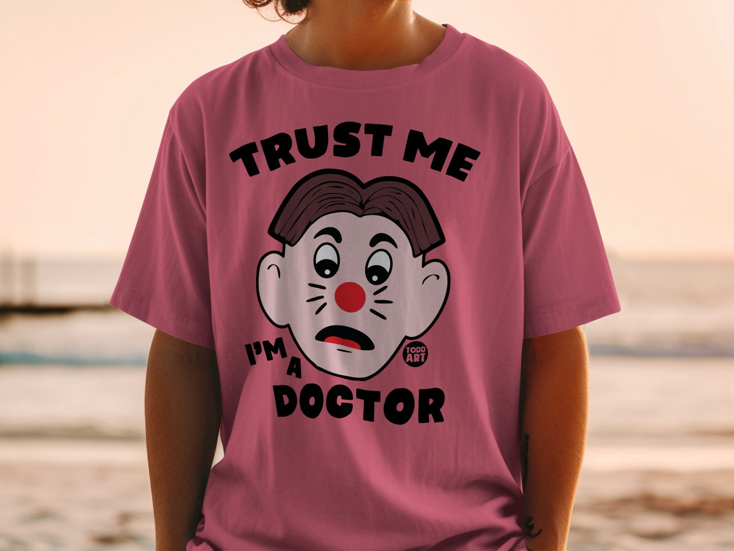 Pink t-shirt with cartoon doctor face and "TRUST ME I'M A DOCTOR" text.
