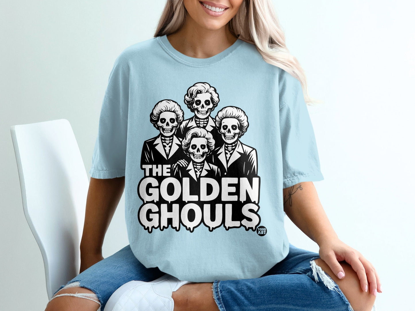 Light blue t-shirt with "The Golden Ghouls" and four skeleton figures.