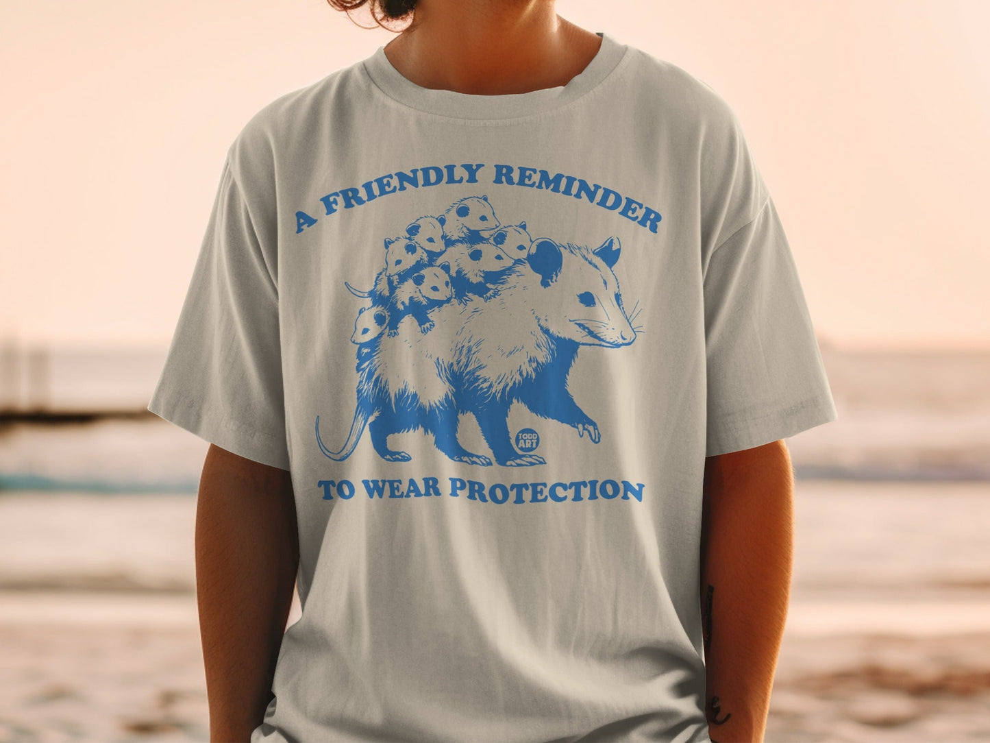 Grey t-shirt with a blue graphic of a possum carrying babies, saying "A Friendly Reminder To Wear Protection".