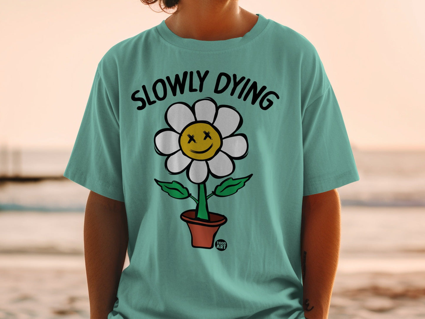 Teal t-shirt with cartoon flower graphic and text "SLOWLY DYING".